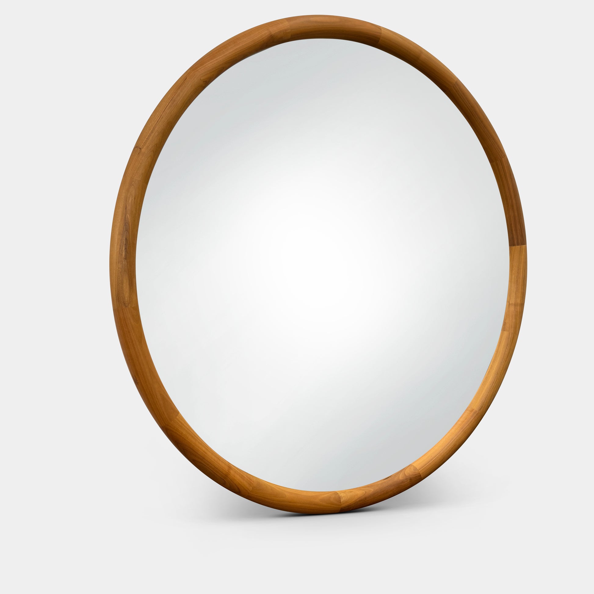 The Round Mirror by Modern Resale features a large wooden frame, reflecting a modern interior with a table, lamps, artwork, and a sculptural wood accent set against white walls and a concrete floor.