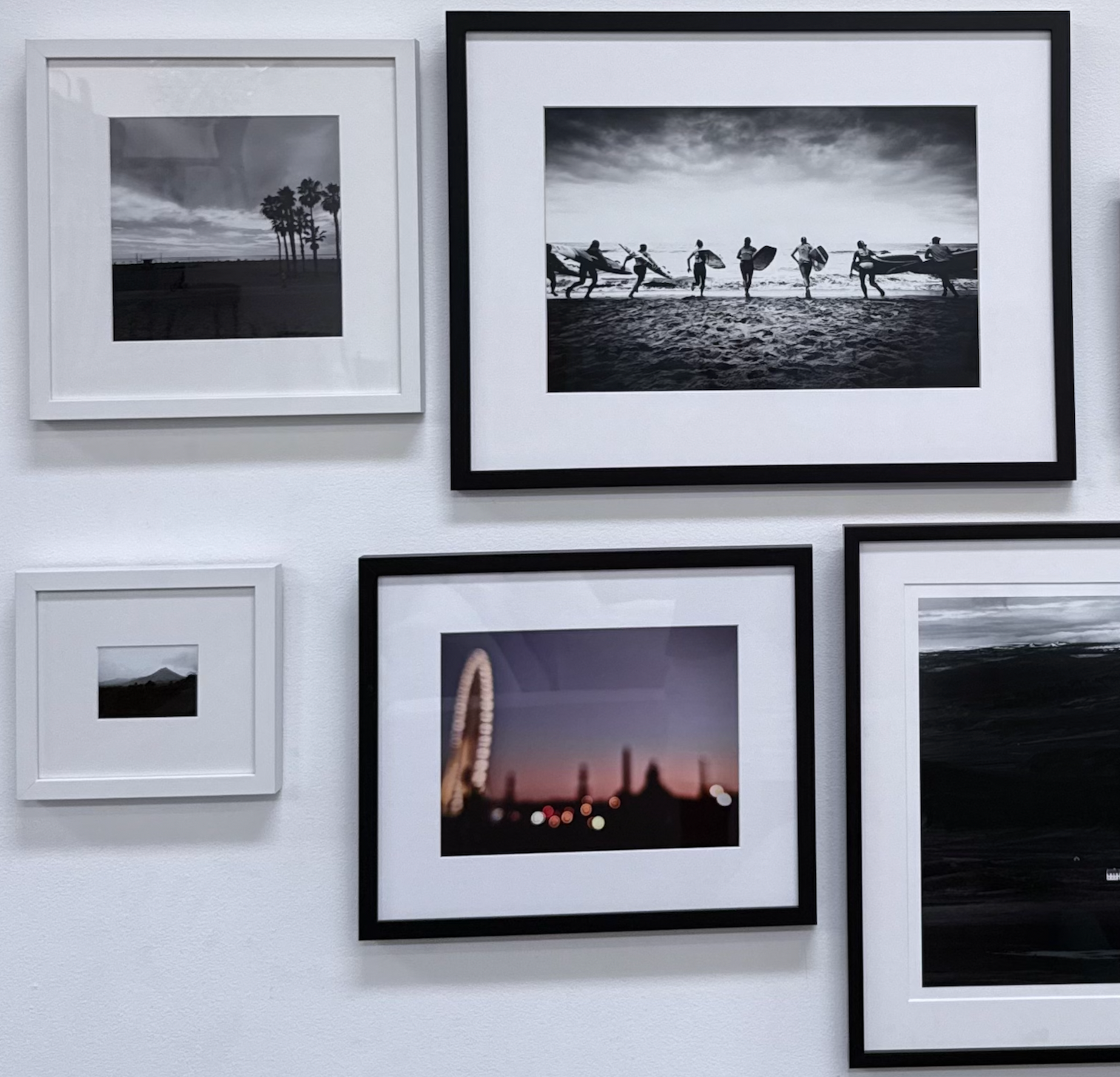 The Set of 5 framed photographs by Modern Resale hangs on a white wall, creating a striking wall decor display. This collection features both black-and-white and color images, showcasing surfers, palm trees, a blurred ferris wheel, and captivating landscapes.