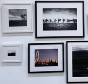 The Set of 5 framed photographs by Modern Resale hangs on a white wall, creating a striking wall decor display. This collection features both black-and-white and color images, showcasing surfers, palm trees, a blurred ferris wheel, and captivating landscapes.