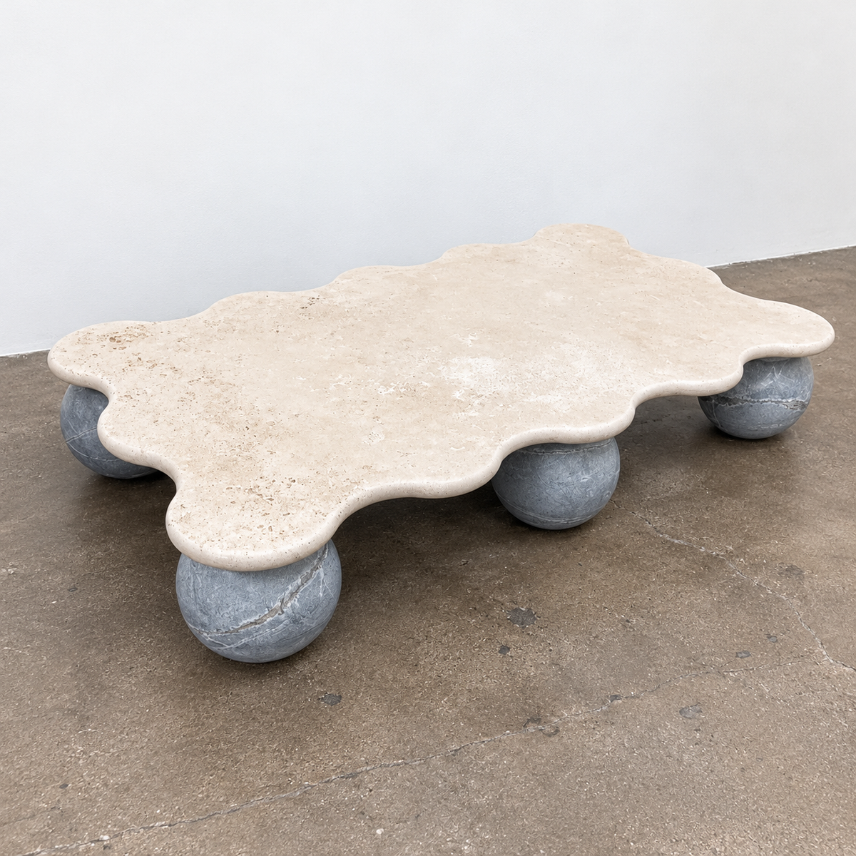 Form(LA) Palla Rectangle Coffee Table with a wavy-edged stone top supported by three spherical stone legs.
