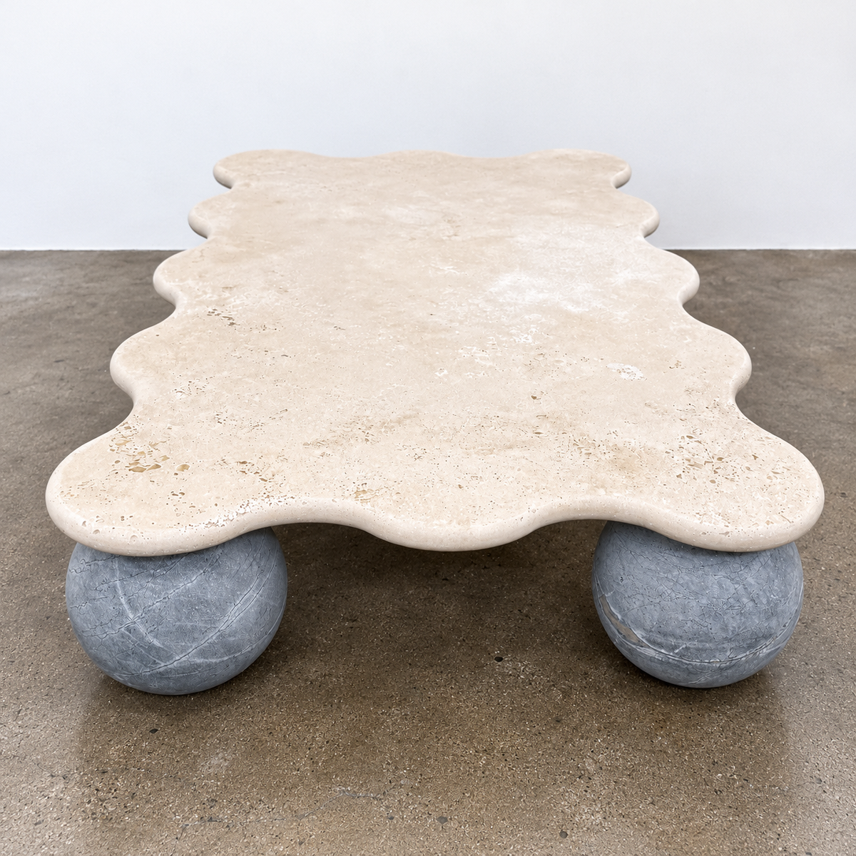 Form(LA) Palla Rectangle Coffee Table with a wavy-edged stone top supported by three spherical stone legs.