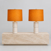 Two Shelter Brasilia Lamp by Modern Resale with textured white bases and orange cylindrical shades are displayed on a beige stone surface against a gray background.