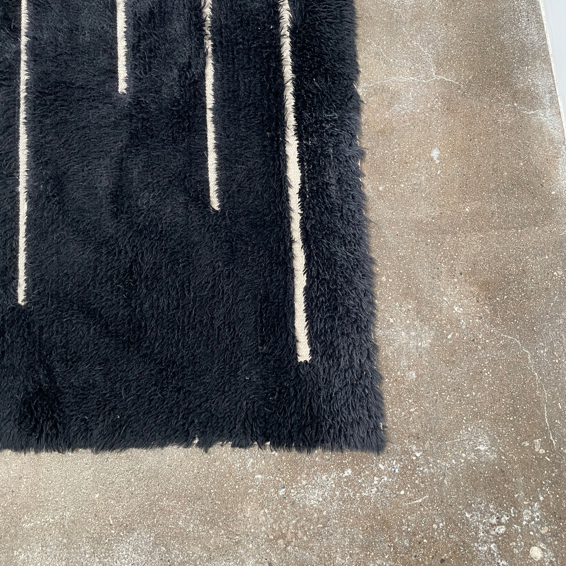 Close-up of a Woven Dilla Black & Ivory wool rug with diagonal white stitching, creating a distinct pattern on a high/low pile surface.