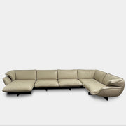 The Cassina Superbeam 5 Piece Leather Sectional in beige, featuring plush cushions, is arranged in a spacious room with white walls, exposed Superbeam ceiling, and overhead lighting.