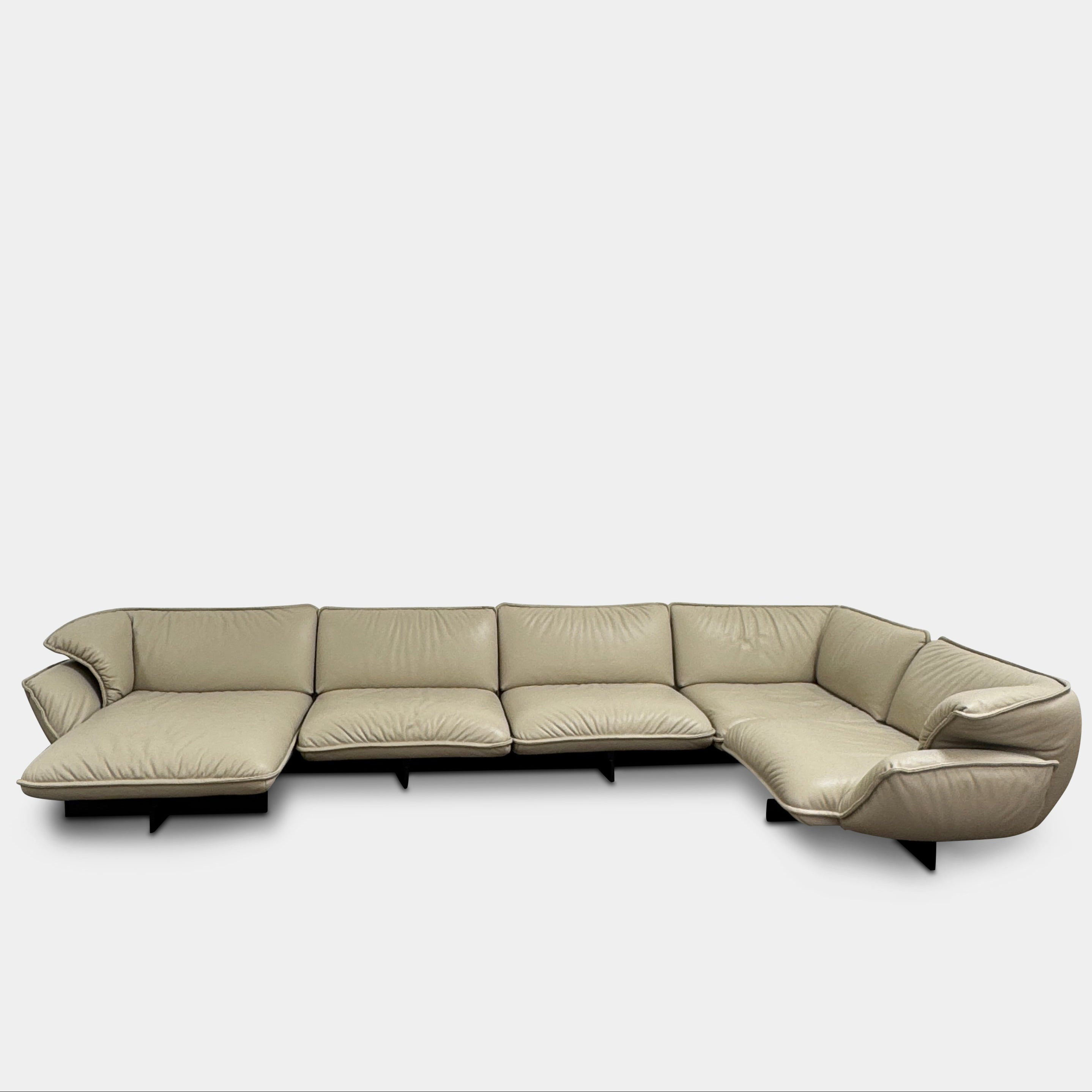 The Cassina Superbeam 5 Piece Leather Sectional in beige, featuring plush cushions, is arranged in a spacious room with white walls, exposed Superbeam ceiling, and overhead lighting.