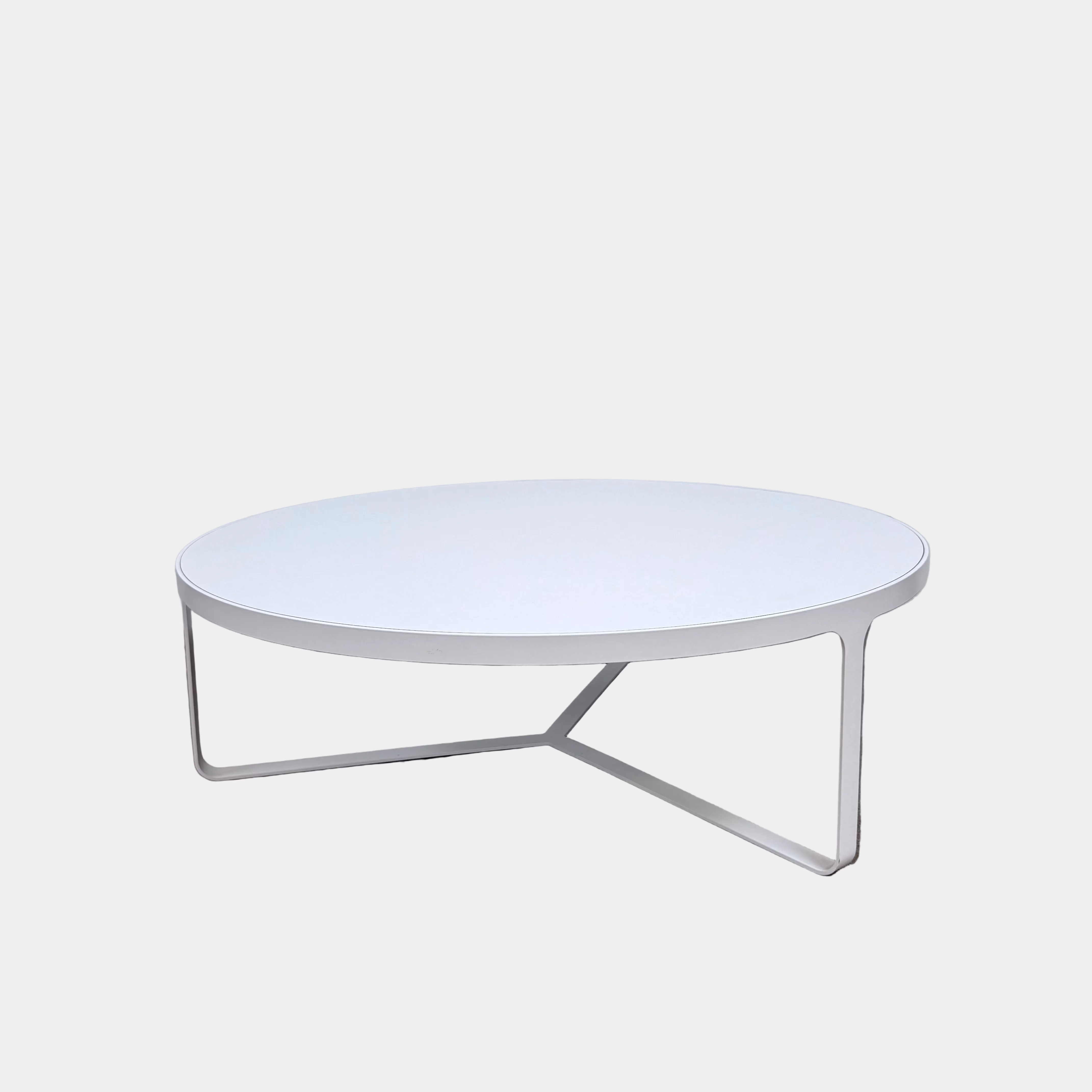 A round Tacchini Cage Coffee Table, White by Tacchini with thin metal legs stands on a plain gray concrete floor against a blank wall.
