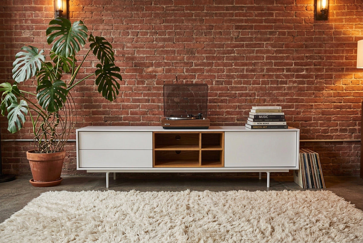 Low-profile white DWR Treku Aura Media Unit on thin legs, featuring two side cabinets and a central open shelf section with a wood-toned interior.