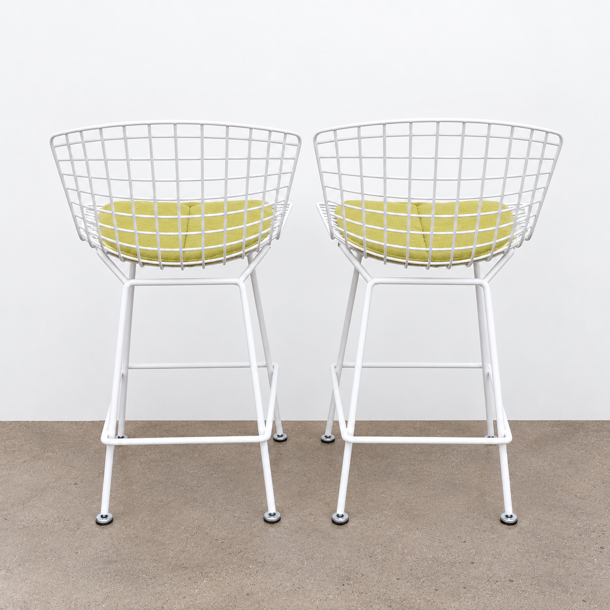Two white Knoll Harry Bertoia Wire Counter Stools with light green seat cushions.