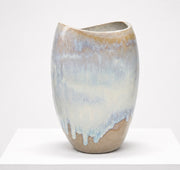 The Sofi Ceramics Florentine Vessel by Artist is a hand-built oval vase with an uneven rim and glossy textured surface, featuring a gradient glaze in soft beige, blue, and white tones displayed on a white pedestal.