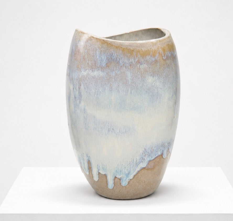 The Sofi Ceramics Florentine Vessel by Artist is a hand-built oval vase with an uneven rim and glossy textured surface, featuring a gradient glaze in soft beige, blue, and white tones displayed on a white pedestal.