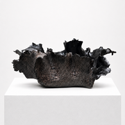 The Sofi Ceramics Black Vessel Wave by Artist, with its dark, jagged edges and irregular form, rests on a white pedestal against a plain backdrop, showcasing the sculptural beauty of this unique vessel.