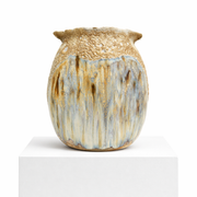 The Sofi Ceramics Vase Spring by Artist is a round, hand-built white clay vase with a textured gold-speckled rim and dripping blue, white, and brown glaze, displayed on a pedestal against a plain background.