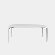 A modern white rectangular B&B Italia LINK Indoor / Outdoor Dining Table by B&B Italia, featuring rounded edges, stands on a brown concrete floor against a plain light gray wall.