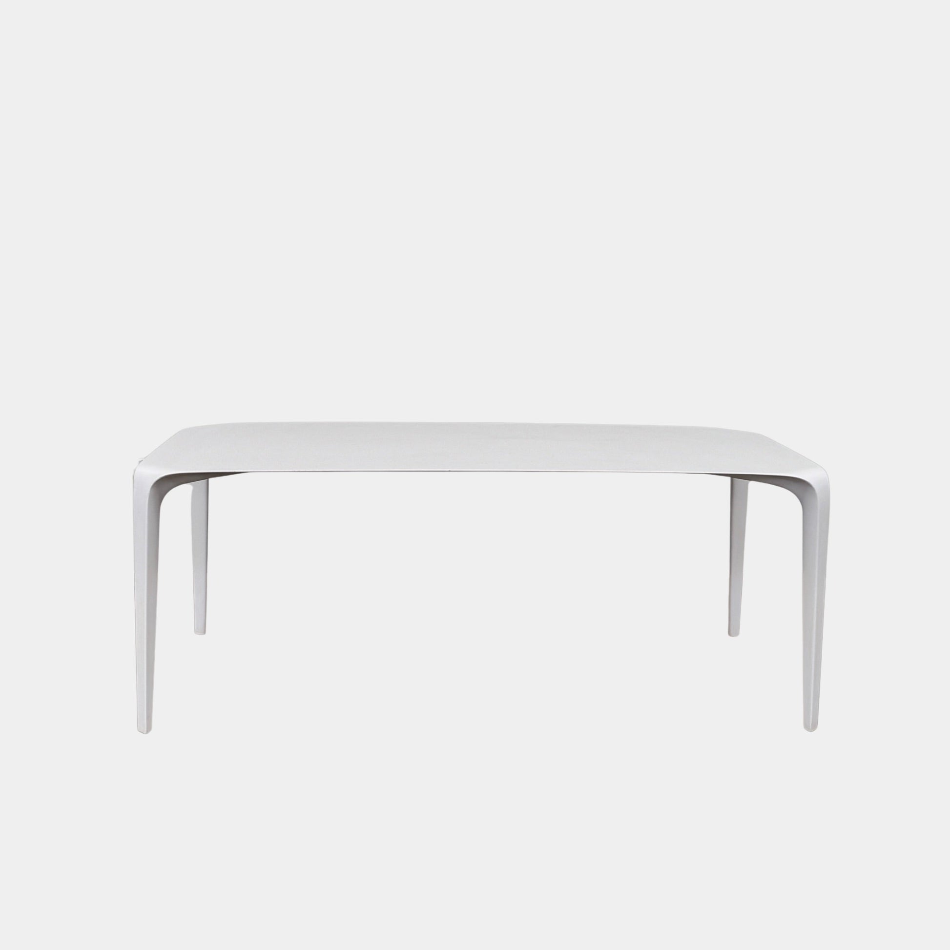 A modern white rectangular B&B Italia LINK Indoor / Outdoor Dining Table by B&B Italia, featuring rounded edges, stands on a brown concrete floor against a plain light gray wall.