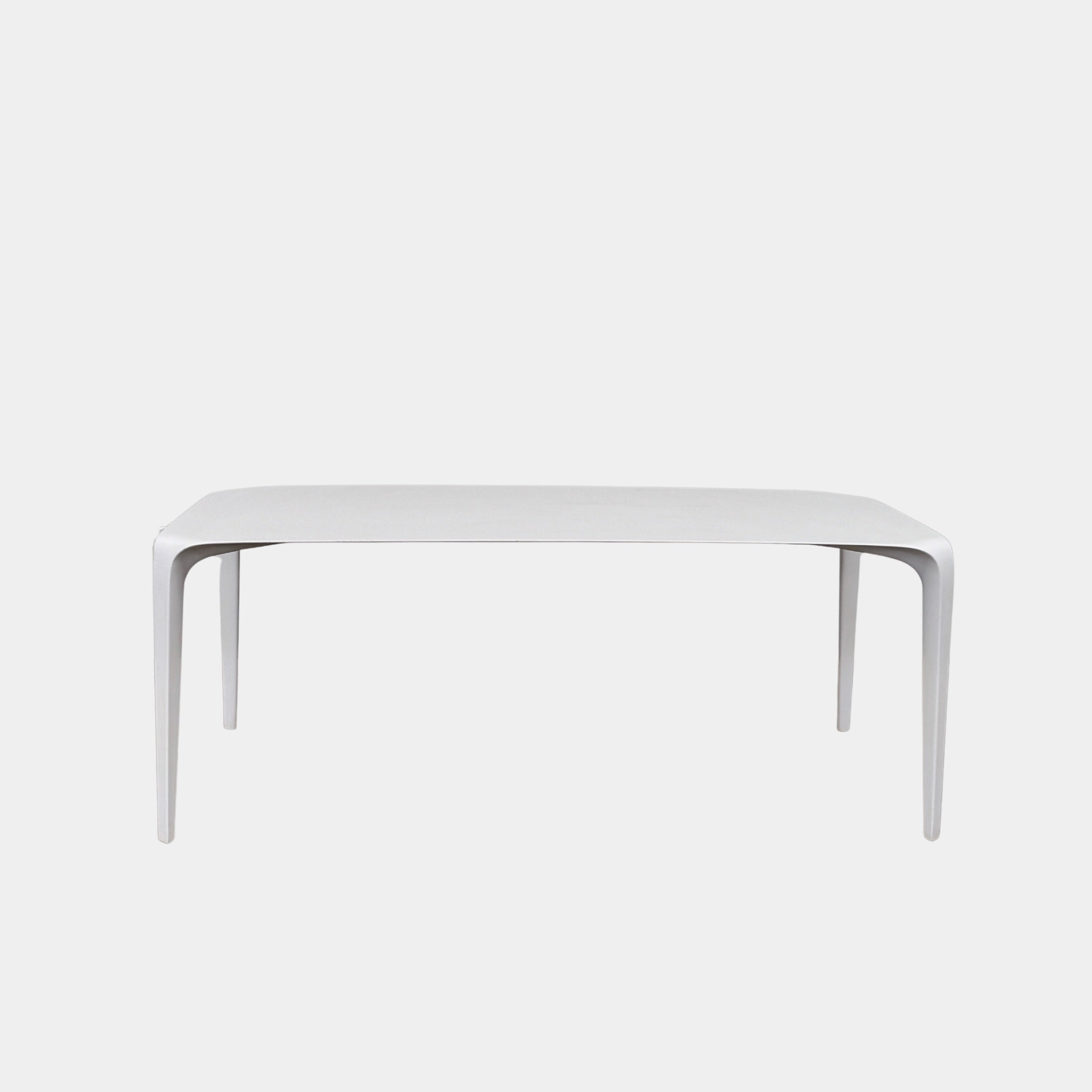 A modern white rectangular B&B Italia LINK Indoor / Outdoor Dining Table by B&B Italia, featuring rounded edges, stands on a brown concrete floor against a plain light gray wall.