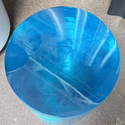 The Jonathan Adler blue acrylic cylindrical table stands upright on a white background, featuring smooth sides and a flat top that evoke the brand’s modern, chic design aesthetic.