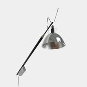 The Ingo Maurer Max Mover Wall Light by Ingo Maurer is a contemporary fixture with an adjustable telescopic rod, sleek black arm, and aluminum reflector in a dome-shaped shade set against a light grey backdrop.