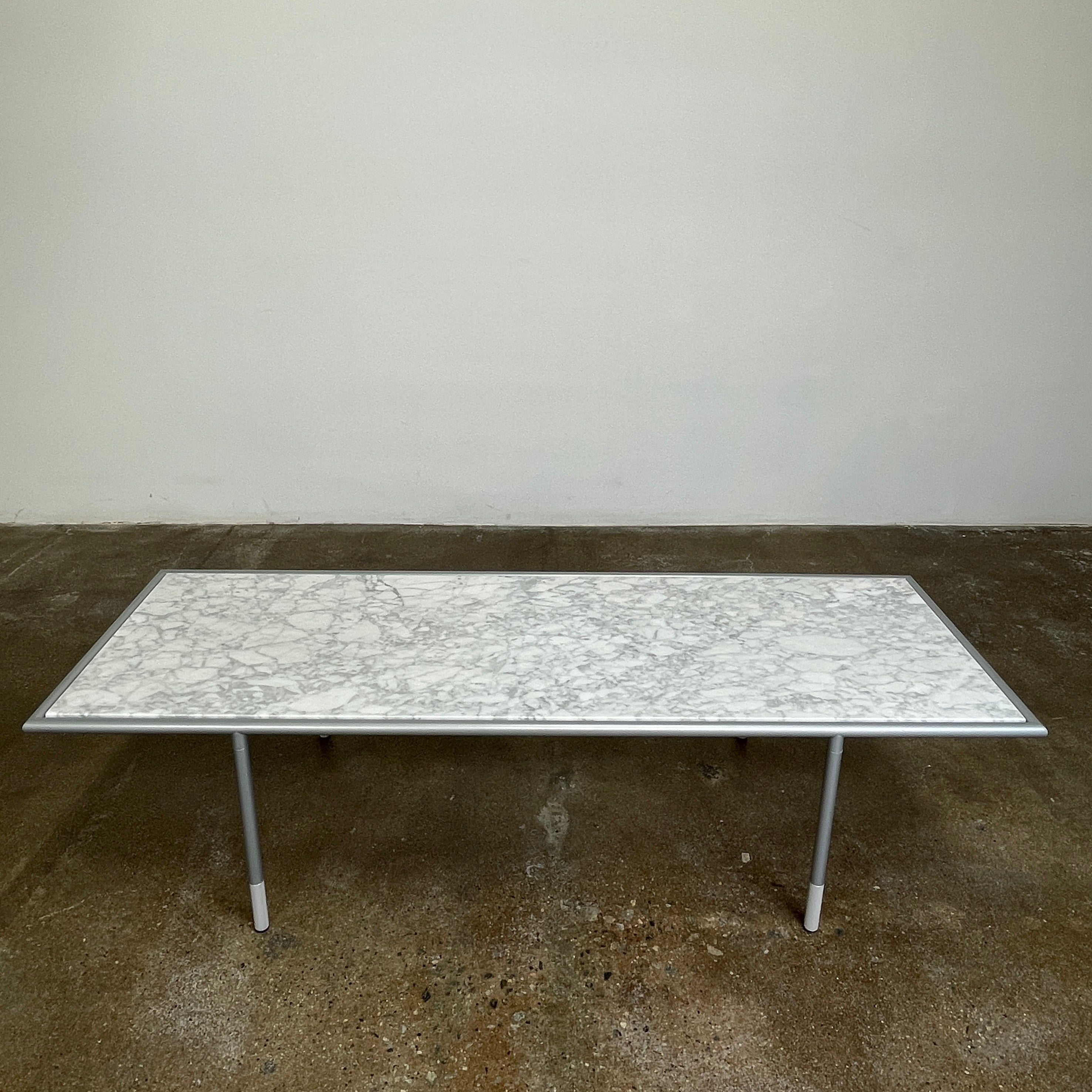 The Artelano Carrara Marble Coffee Table boasts a rectangular marble top with sleek metal legs and a central wood tray, exuding the Parisian elegance of the Artelano brand.