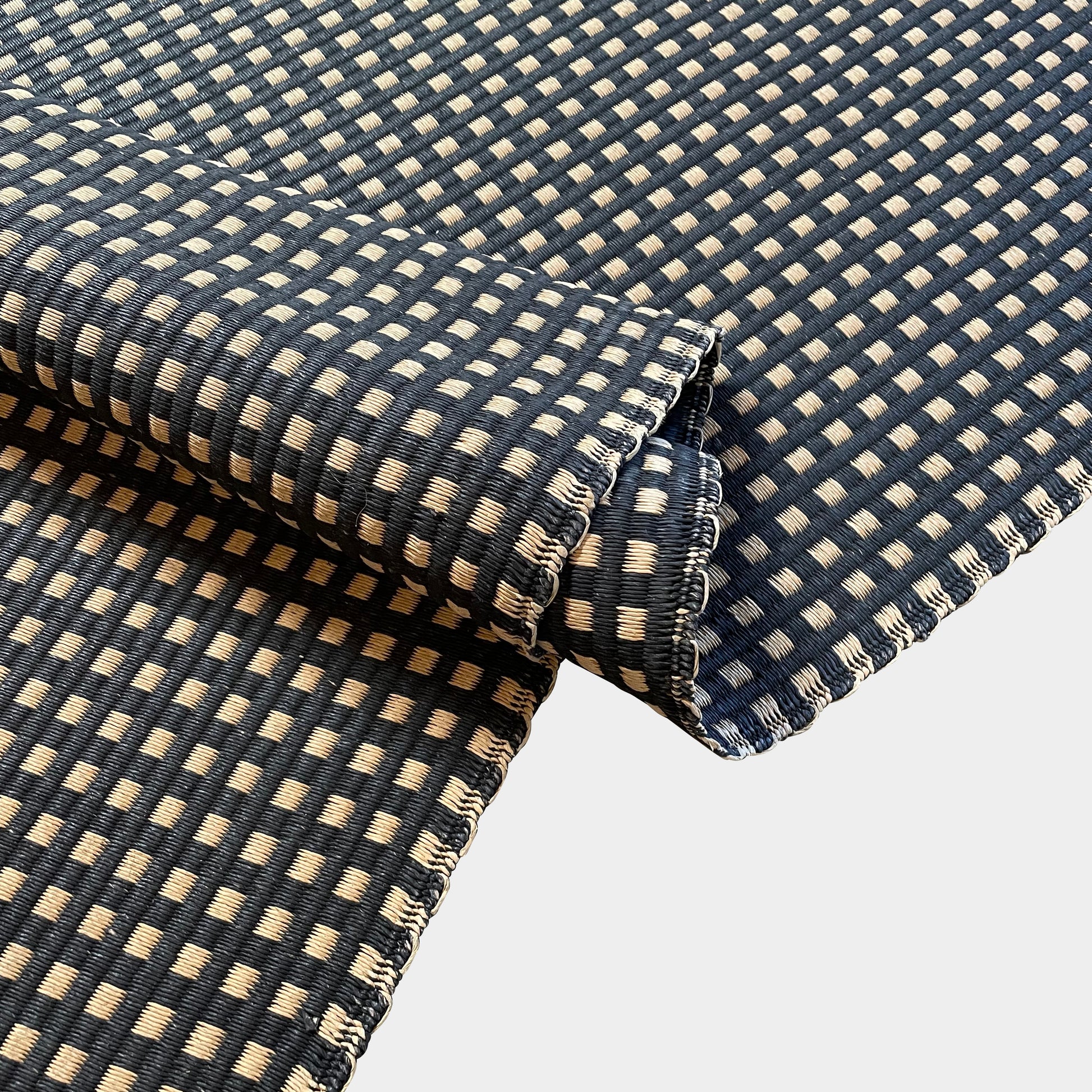 An indoor/outdoor Woodnotes City Rug with cozy detail, in black and tan, on a white surface.