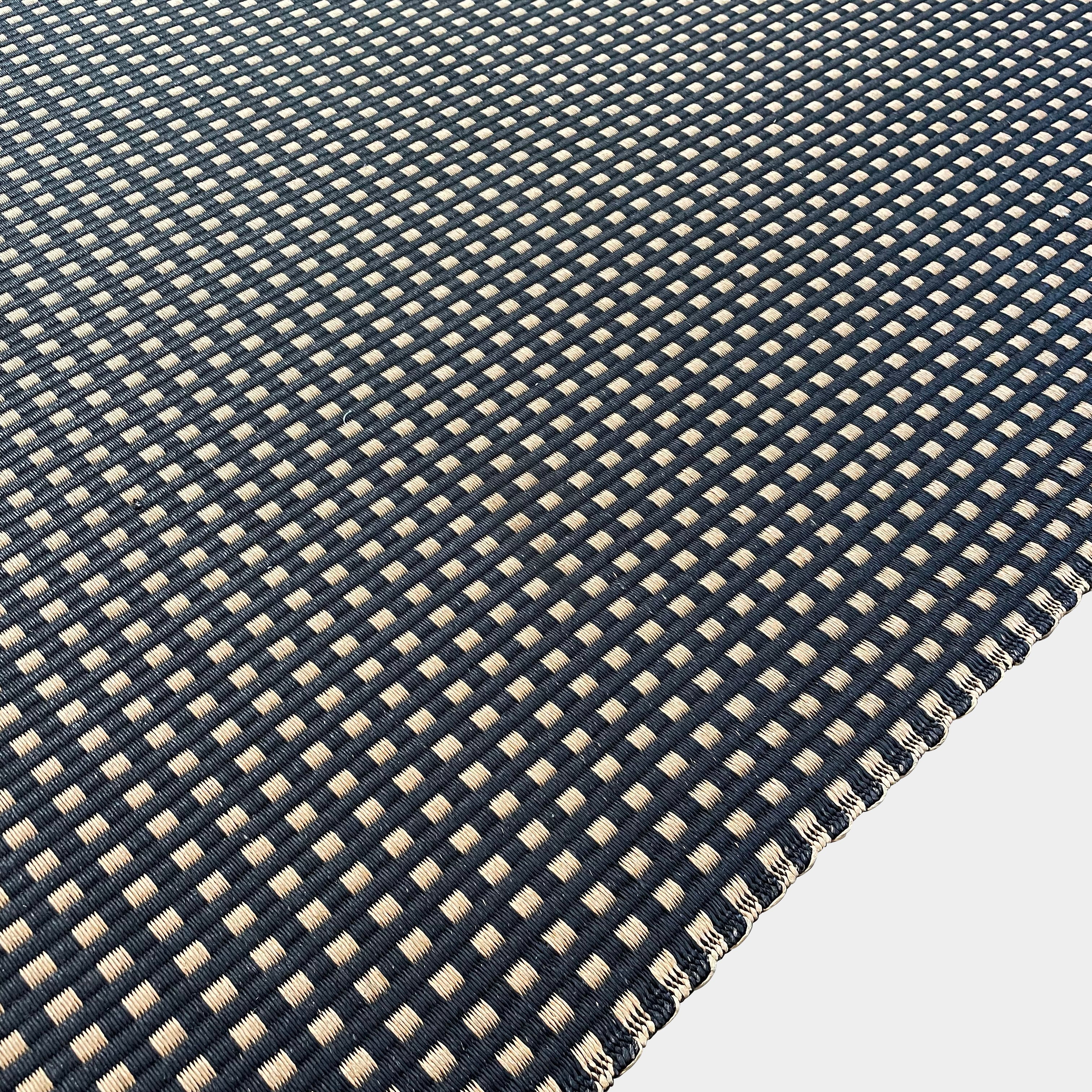 An indoor/outdoor Woodnotes City Rug with cozy detail, in black and tan, on a white surface.