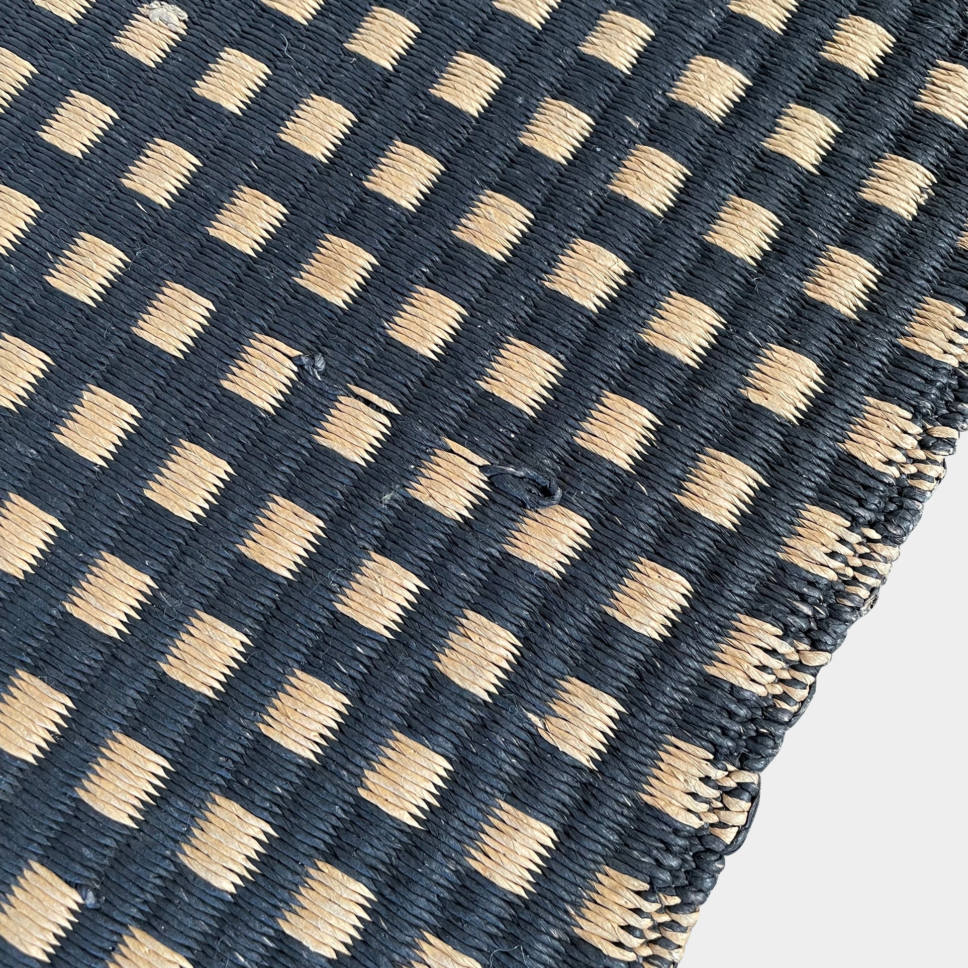 An indoor/outdoor Woodnotes City Rug with cozy detail, in black and tan, on a white surface.