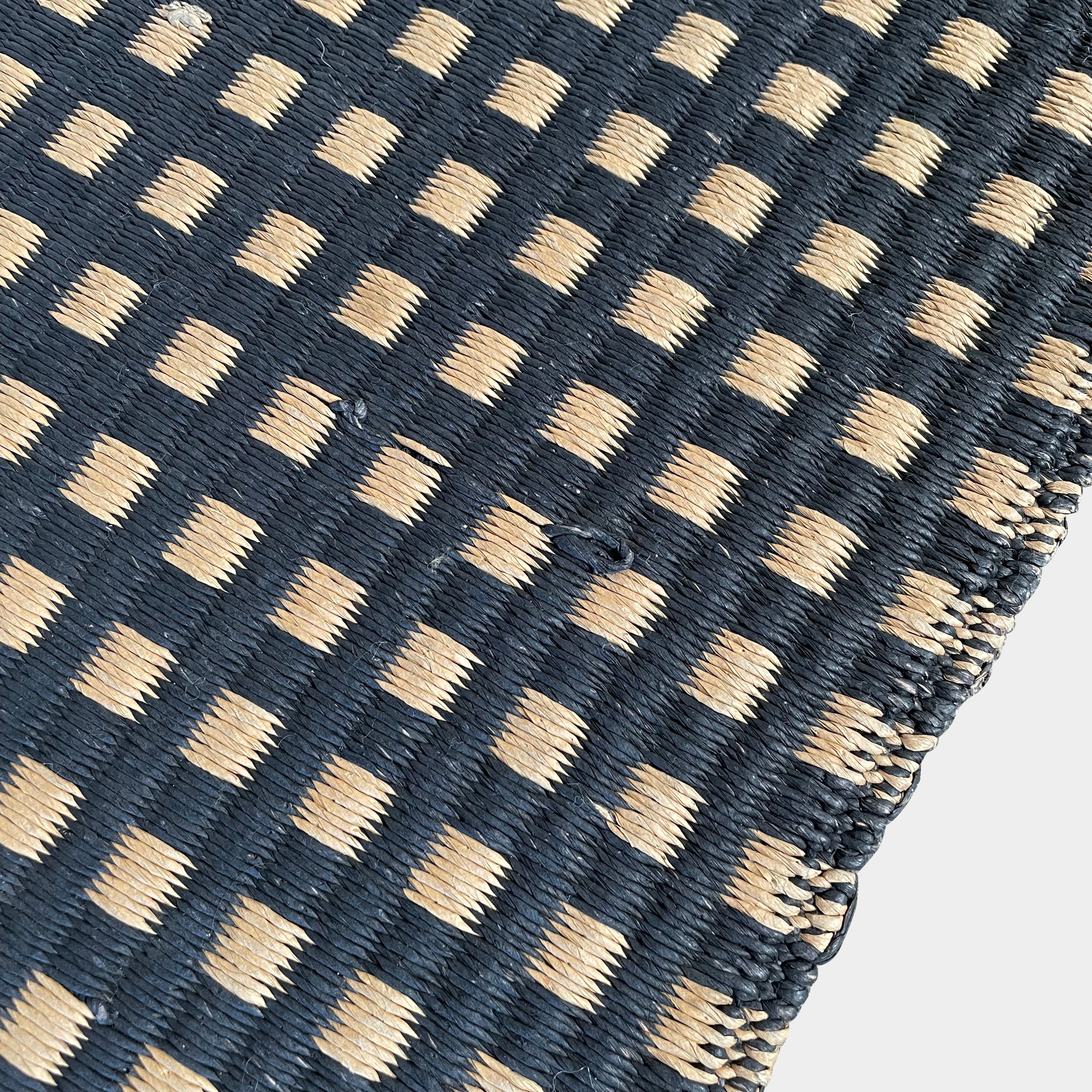 An indoor/outdoor Woodnotes City Rug with cozy detail, in black and tan, on a white surface.