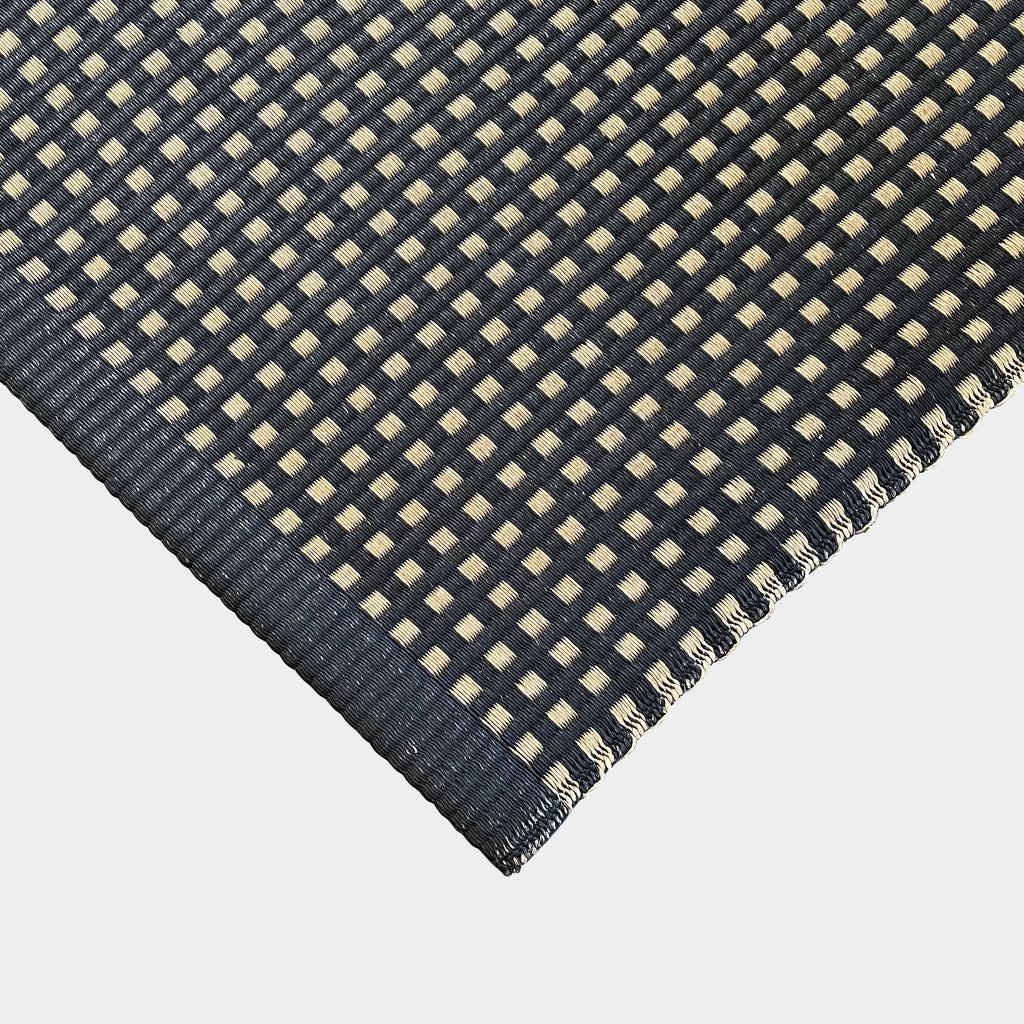 An indoor/outdoor Woodnotes City Rug with cozy detail, in black and tan, on a white surface.