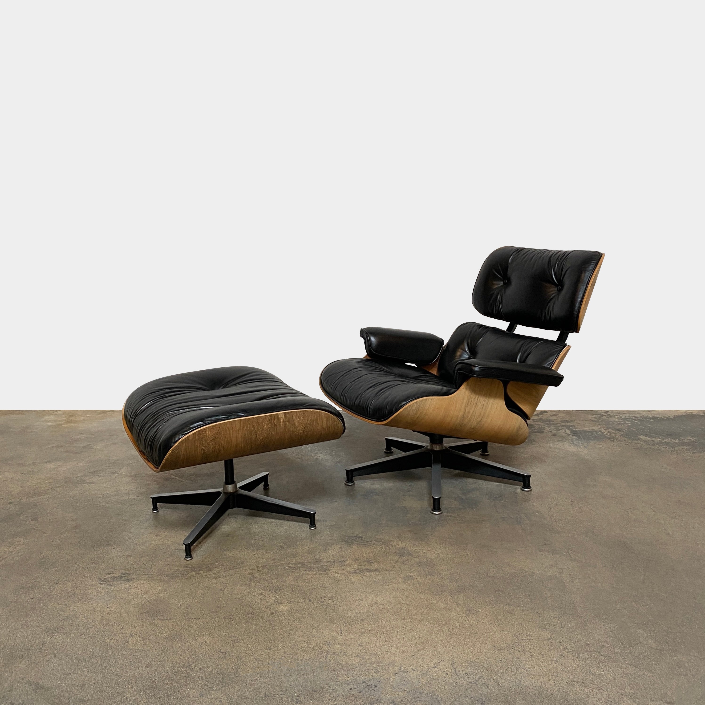 The MillerKnoll Herman Miller Eames Lounge Chair & Ottoman features black leather, wooden frames, and metal swivel bases, showcased against a white background—a timeless modern classic for sophisticated interiors.