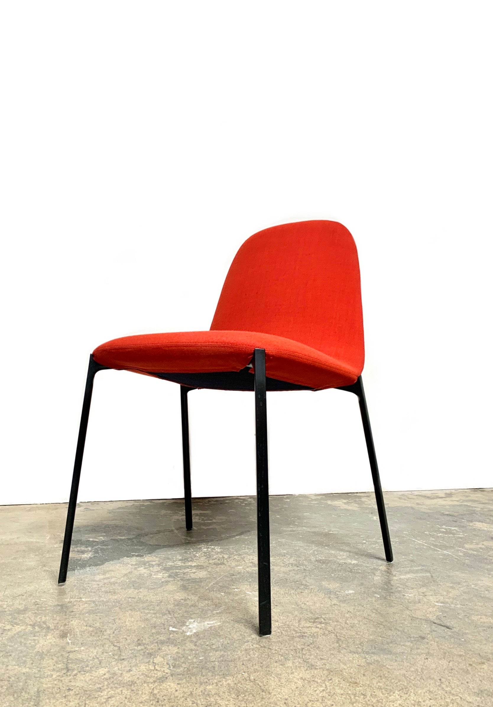 Four Zanotta Ella Dining Chairs, with their red fabric and black metal legs, are set in a row against a plain white background, showcasing the sleek design of this Italian brand.