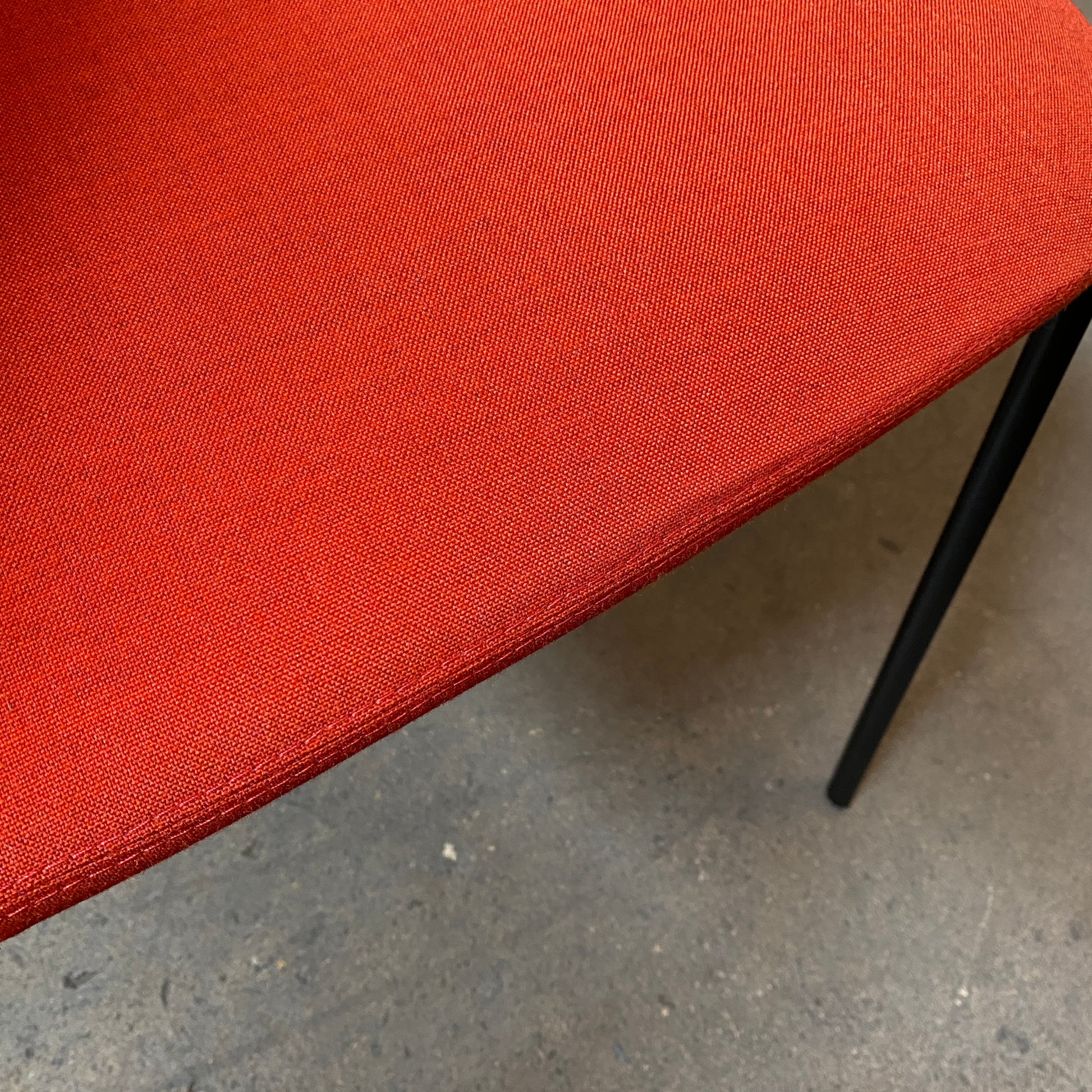 Four Zanotta Ella Dining Chairs, with their red fabric and black metal legs, are set in a row against a plain white background, showcasing the sleek design of this Italian brand.