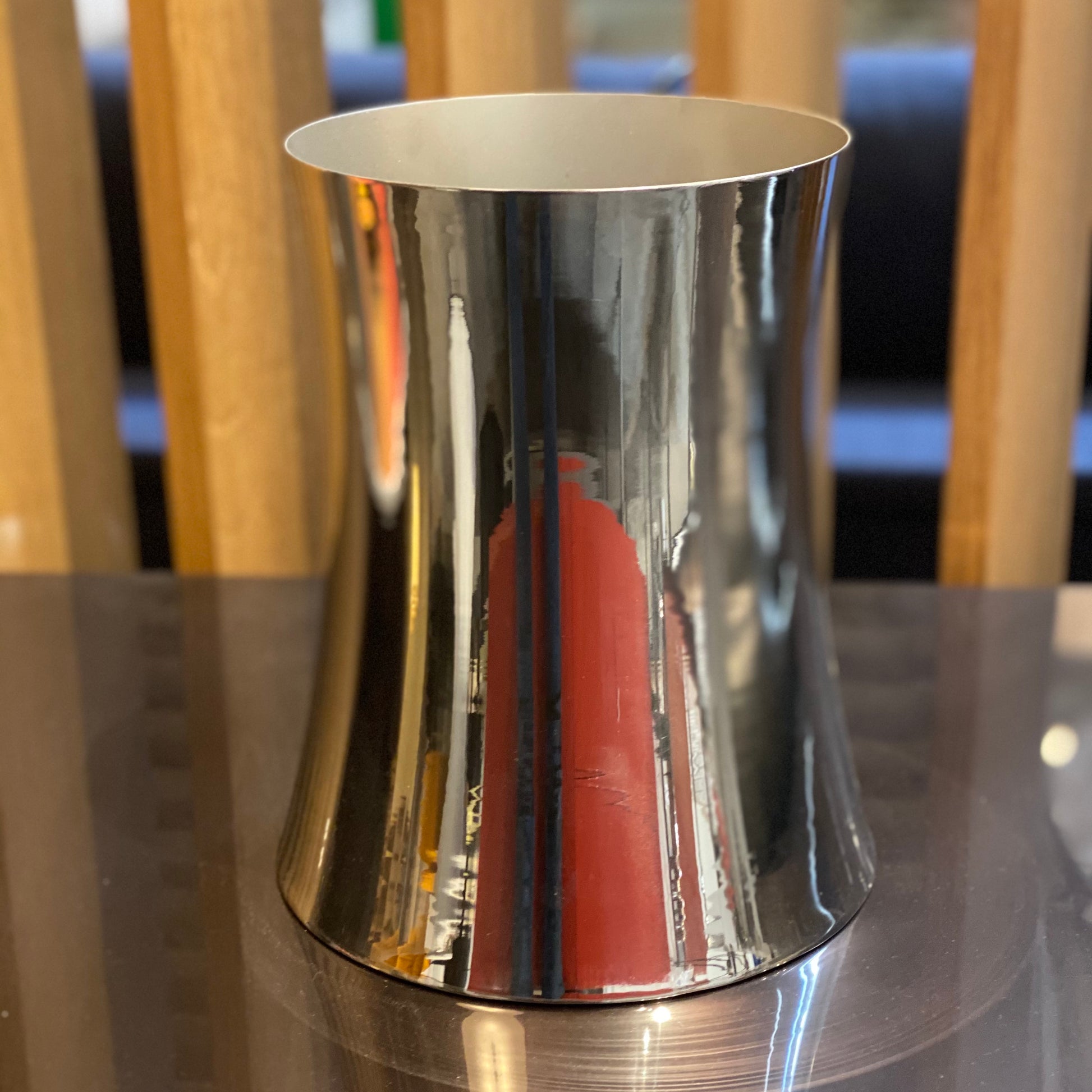 The Zubazuba Vessel by Leo Aerts, from Alinea Design Objects, is crafted from polished stainless steel with a subtly concave middle design. It stands elegantly upright against a simple backdrop, showcasing its versatility as both an artistic piece and a sophisticated champagne bucket.