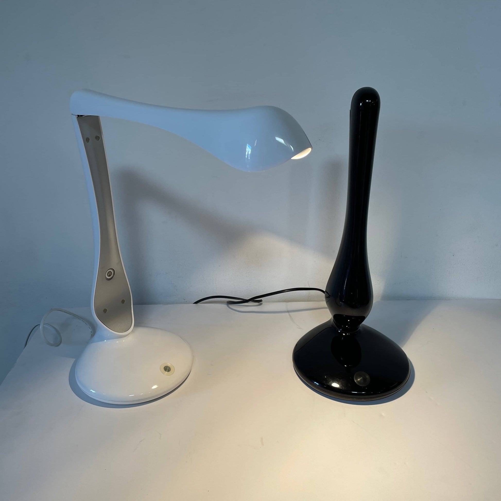 A modern white desk lamp with a curved design and a round base, reminiscent of Ross Lovegrove's aesthetic, akin to the elegance of Yamagiwa Geon Task Lights by Yamagiwa.