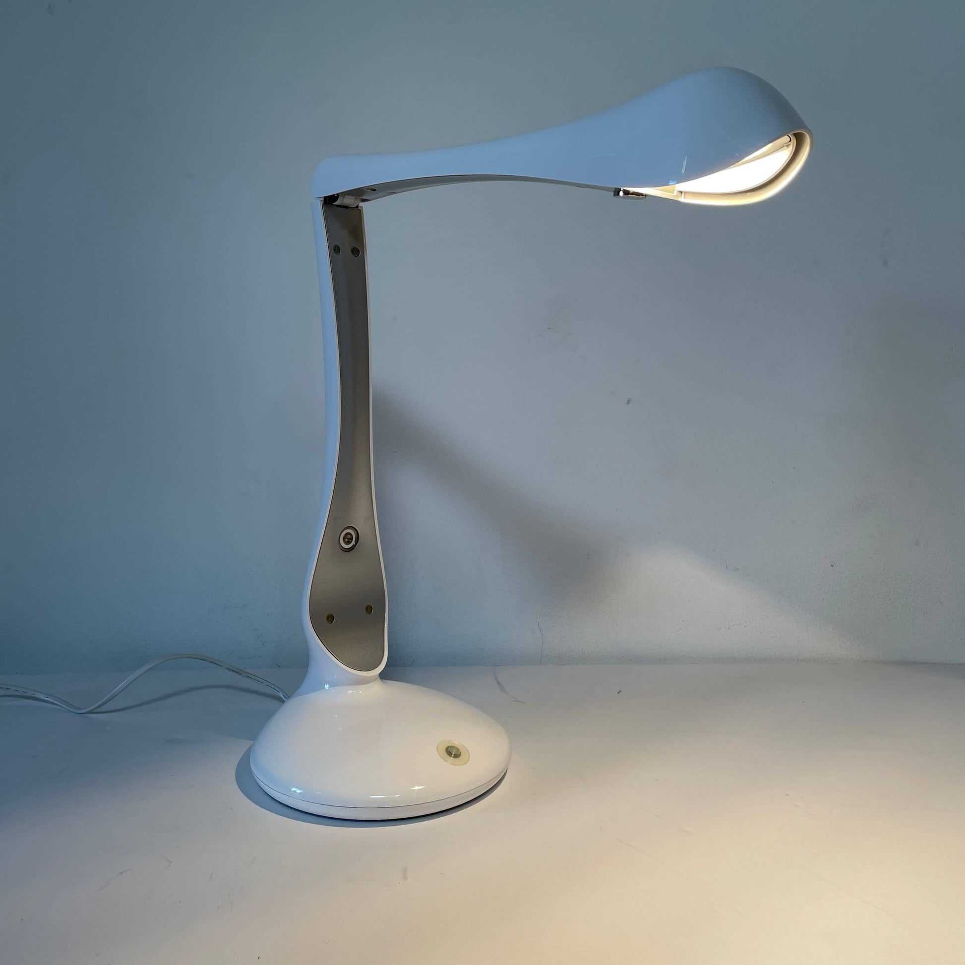 A modern white desk lamp with a curved design and a round base, reminiscent of Ross Lovegrove's aesthetic, akin to the elegance of Yamagiwa Geon Task Lights by Yamagiwa.