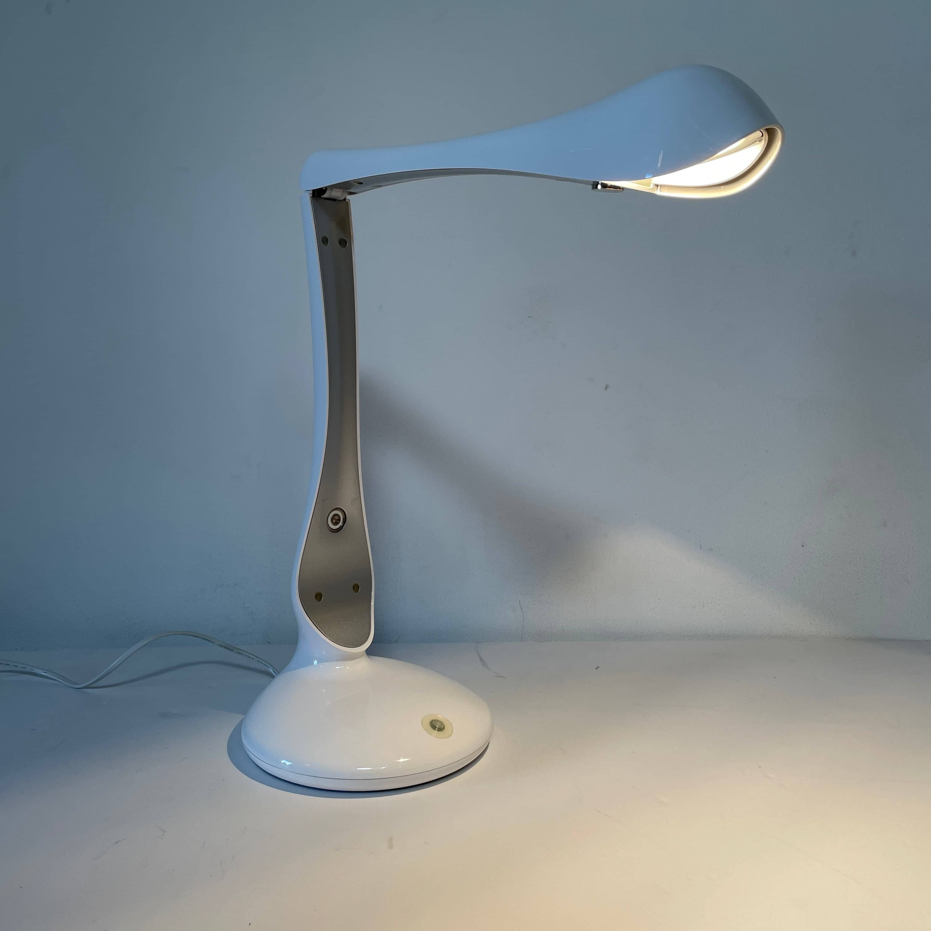 A modern white desk lamp with a curved design and a round base, reminiscent of Ross Lovegrove's aesthetic, akin to the elegance of Yamagiwa Geon Task Lights by Yamagiwa.