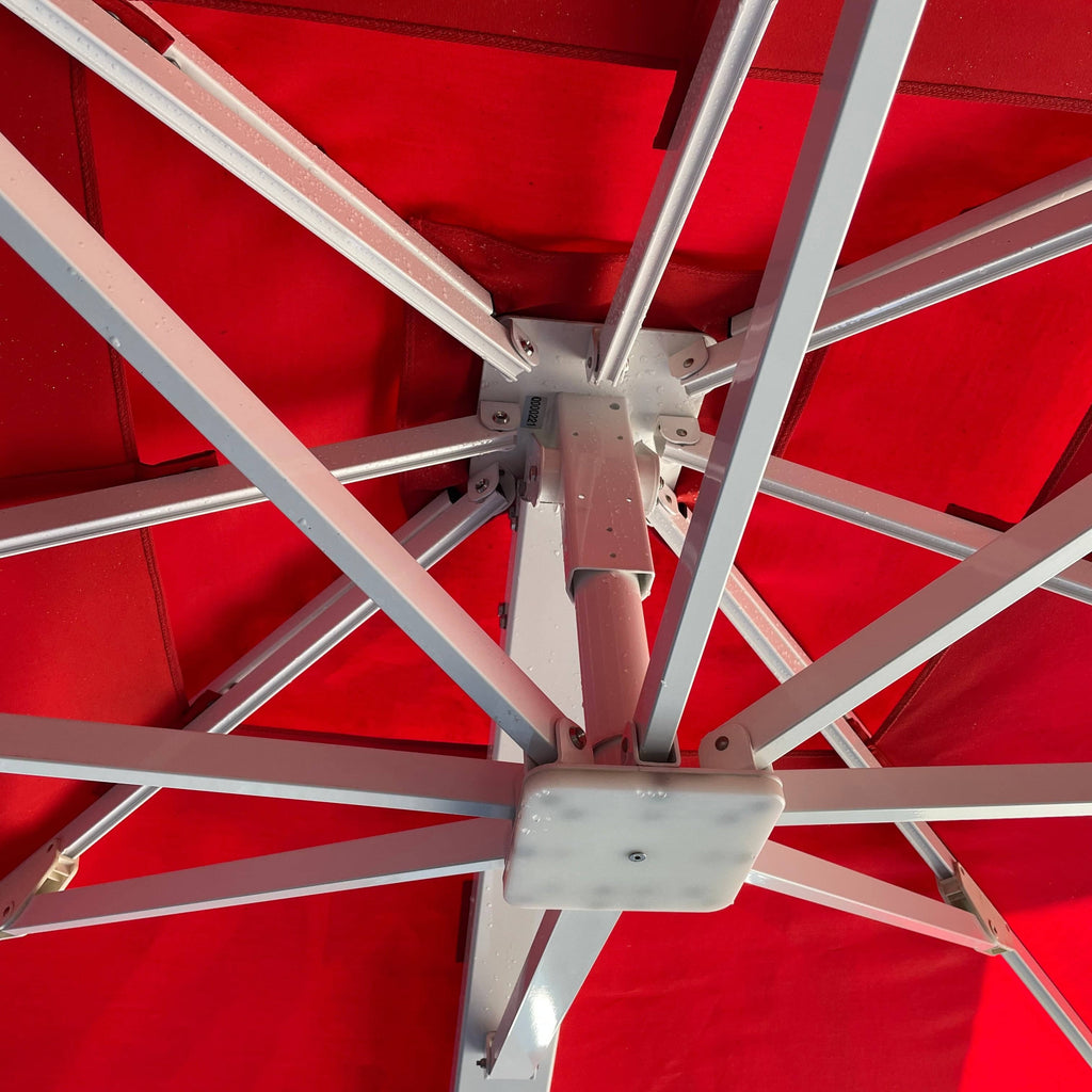 A red Crema Diomede outdoor umbrella on a stand with a white background.