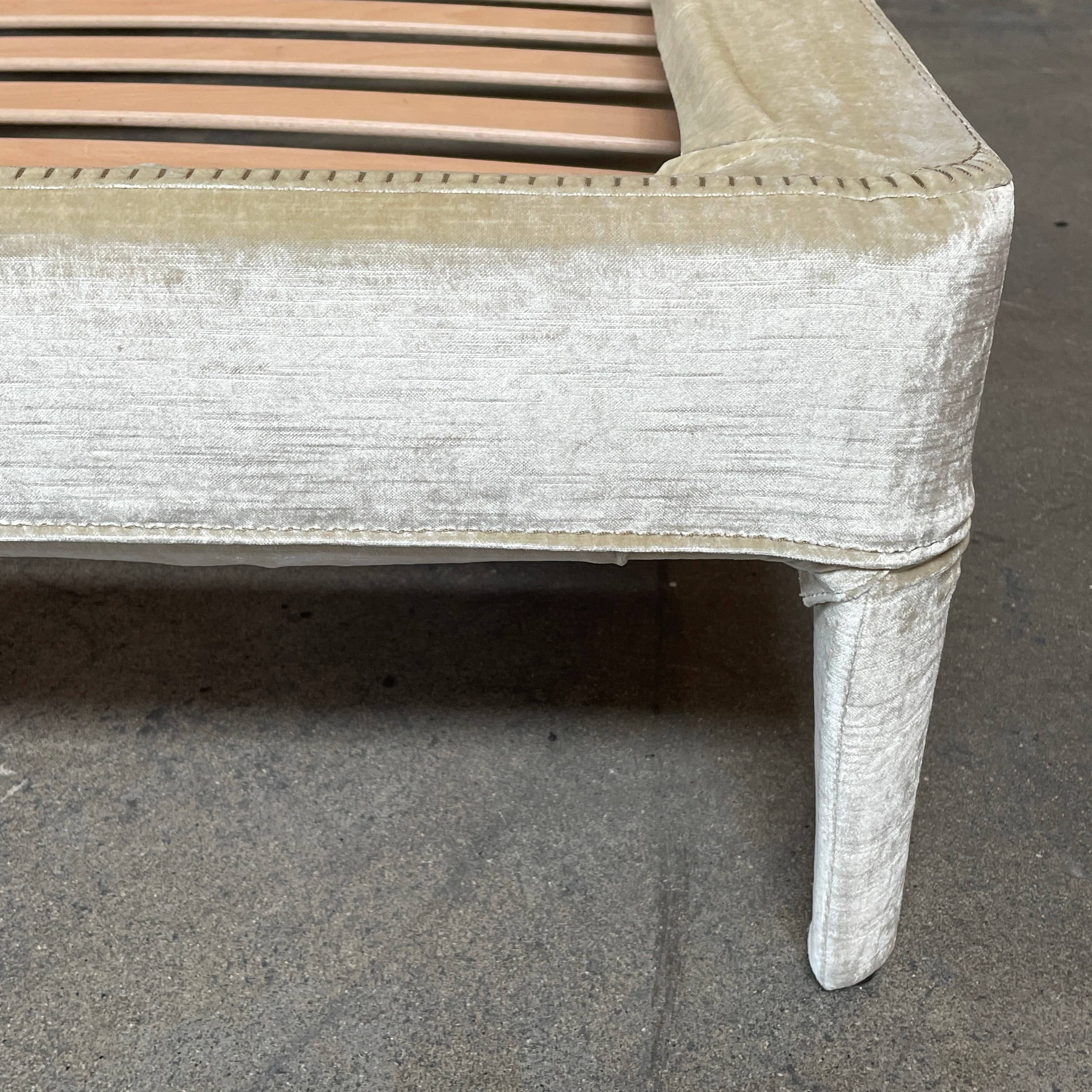 The Maxalto Febo Queen Bed is an upholstered bed frame featuring a headboard and two pillows, all elegantly wrapped in champagne-colored velvet. The frame boasts wooden slats for support, providing the refined touch of a luxury hotel bed. Shown without a mattress.