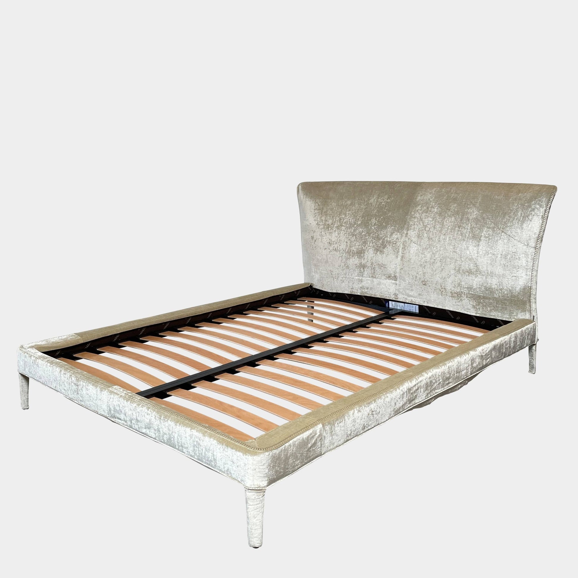 The Maxalto Febo Queen Bed is an upholstered bed frame featuring a headboard and two pillows, all elegantly wrapped in champagne-colored velvet. The frame boasts wooden slats for support, providing the refined touch of a luxury hotel bed. Shown without a mattress.