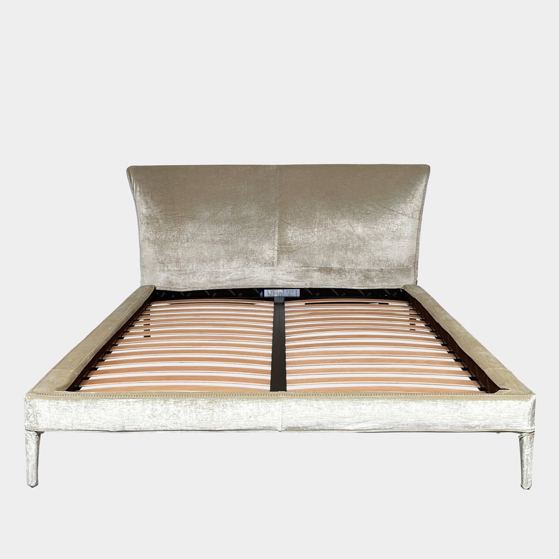 The Maxalto Febo Queen Bed is an upholstered bed frame featuring a headboard and two pillows, all elegantly wrapped in champagne-colored velvet. The frame boasts wooden slats for support, providing the refined touch of a luxury hotel bed. Shown without a mattress.