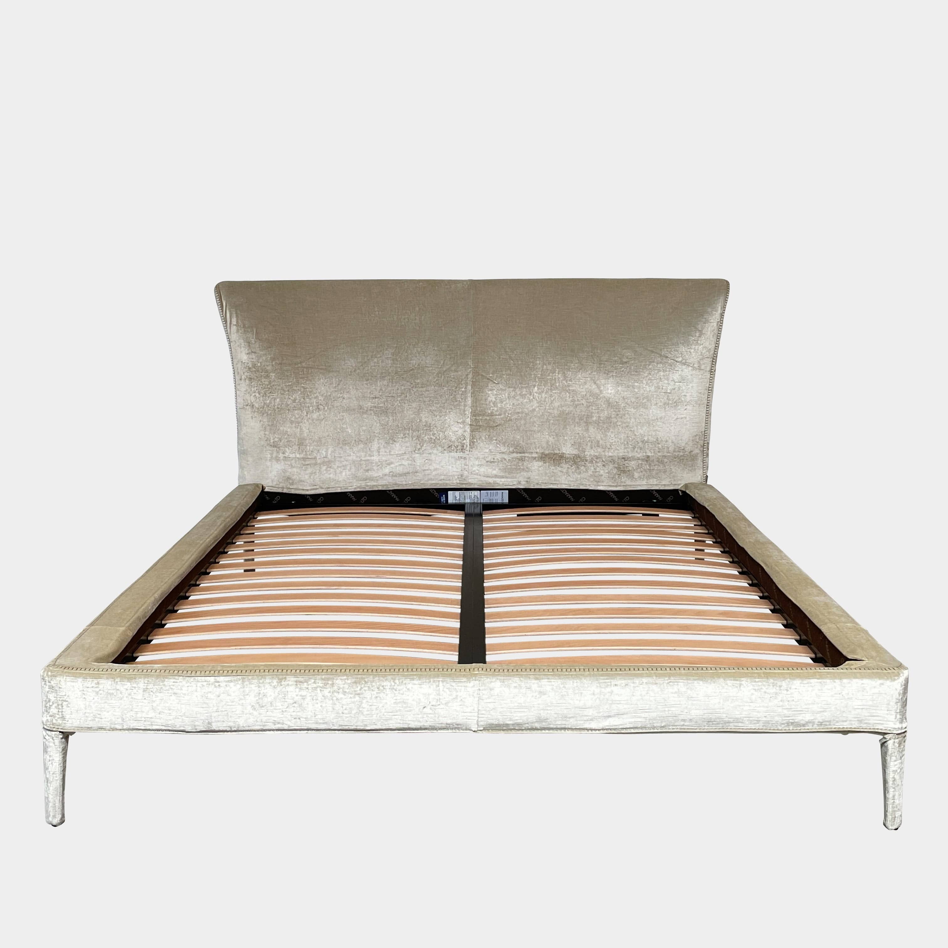 The Maxalto Febo Queen Bed is an upholstered bed frame featuring a headboard and two pillows, all elegantly wrapped in champagne-colored velvet. The frame boasts wooden slats for support, providing the refined touch of a luxury hotel bed. Shown without a mattress.