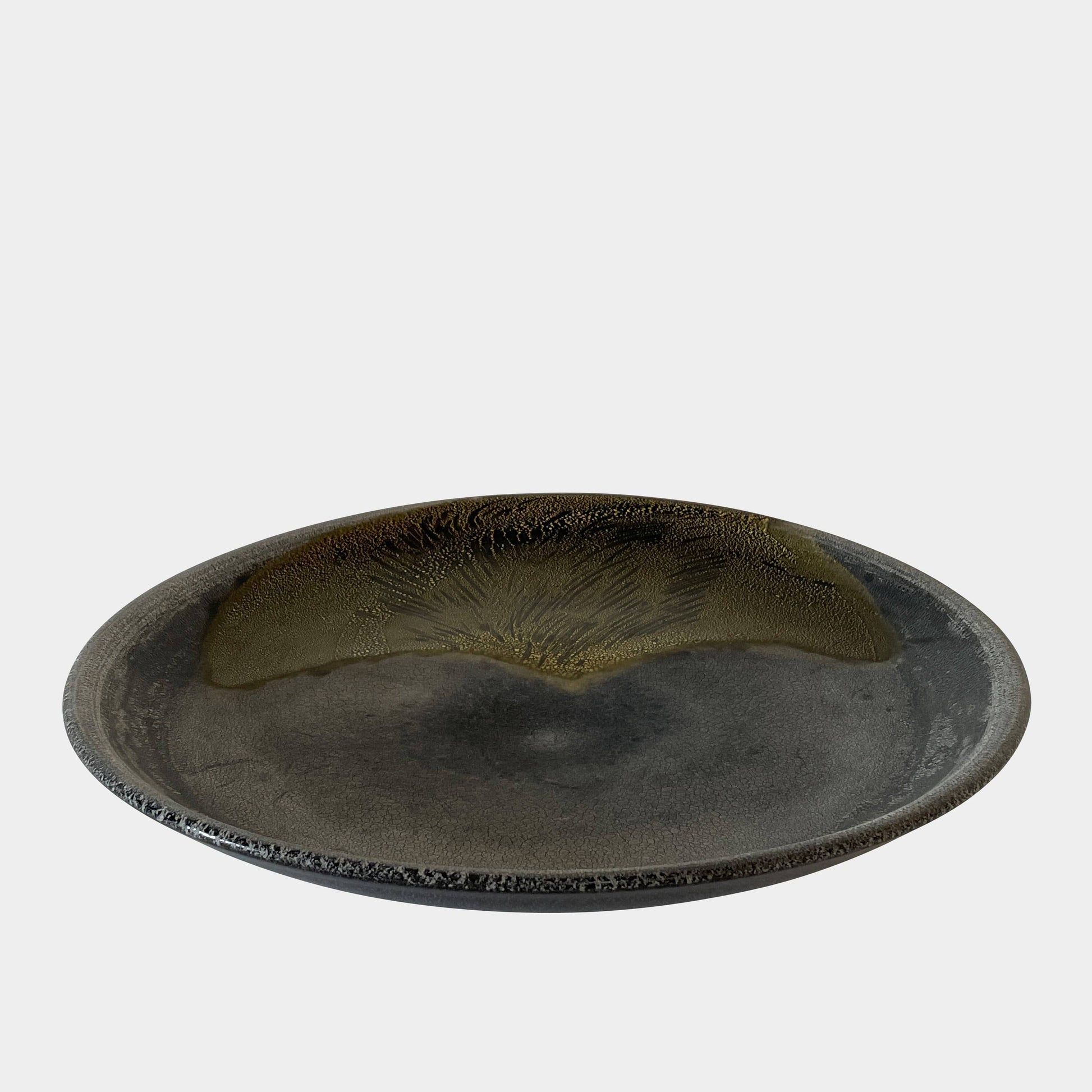 A round ceramic plate featuring a central raised circular design, predominantly gray with earthy bronze tones and textured streaks on one side, reminiscent of the artistry seen in the Alfredo Barbini Murano Glass Plate And Object.