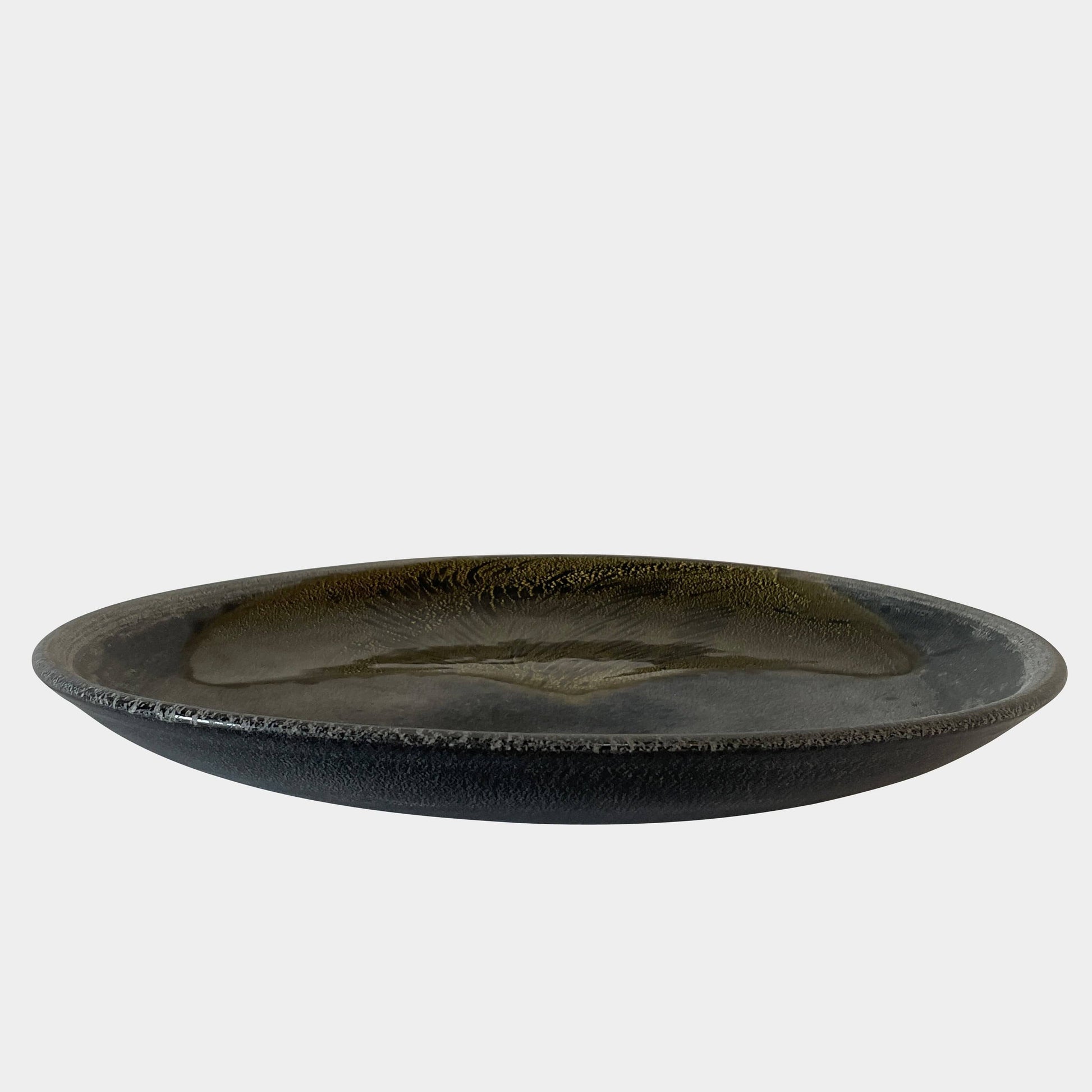 A round ceramic plate featuring a central raised circular design, predominantly gray with earthy bronze tones and textured streaks on one side, reminiscent of the artistry seen in the Alfredo Barbini Murano Glass Plate And Object.