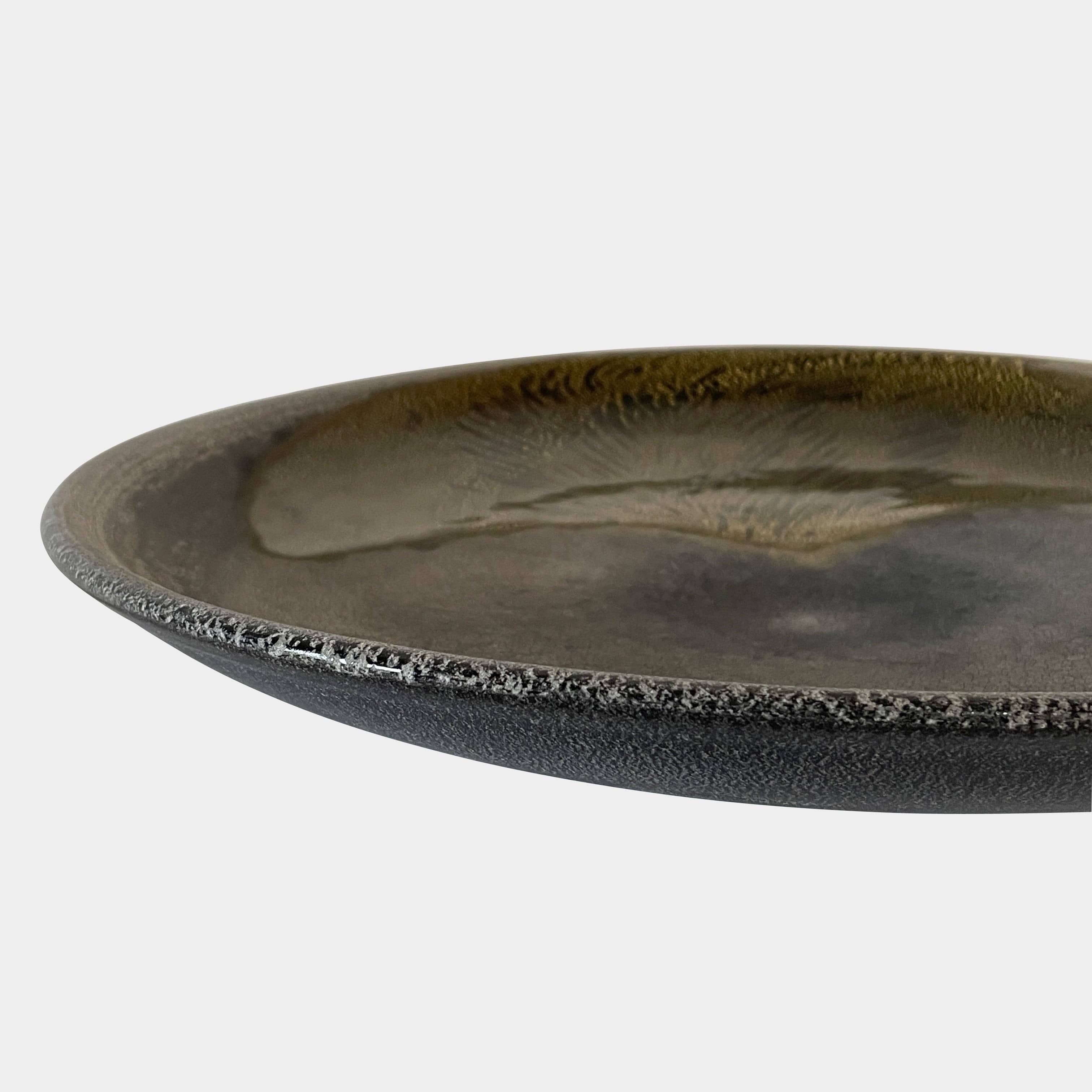 A round ceramic plate featuring a central raised circular design, predominantly gray with earthy bronze tones and textured streaks on one side, reminiscent of the artistry seen in the Alfredo Barbini Murano Glass Plate And Object.
