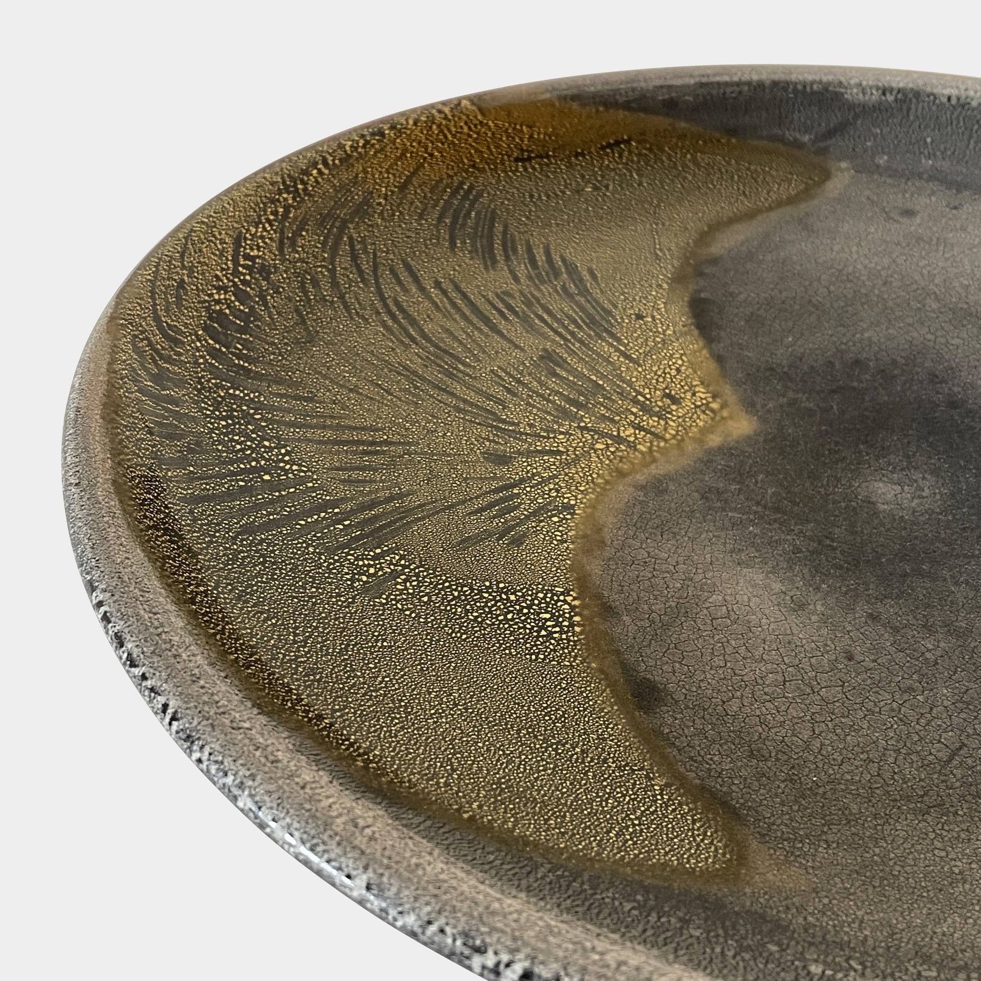 A round ceramic plate featuring a central raised circular design, predominantly gray with earthy bronze tones and textured streaks on one side, reminiscent of the artistry seen in the Alfredo Barbini Murano Glass Plate And Object.