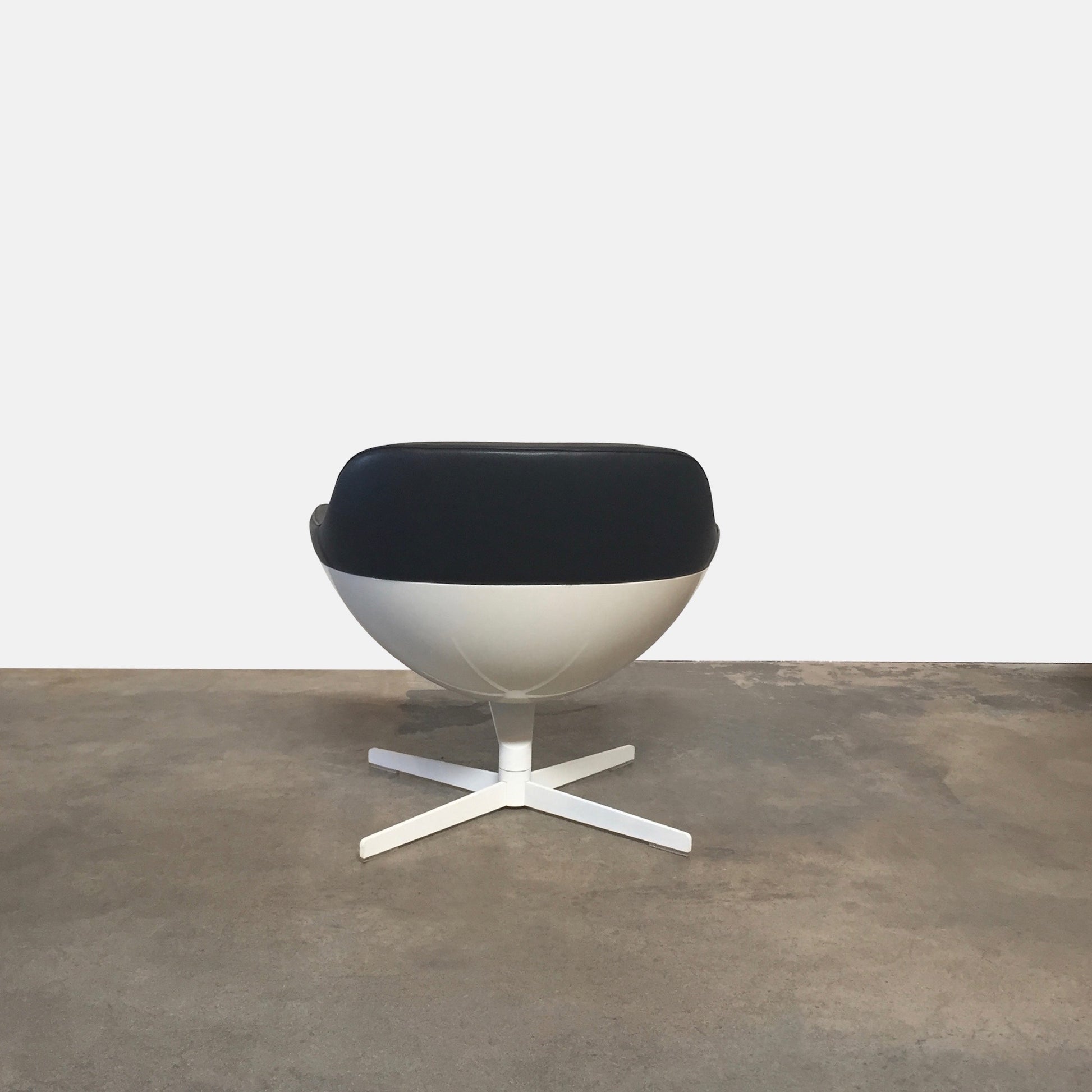 Cassina Auckland Swivel Lounge Chair by Jean-Marie Massaud, featuring a modern black and white curved seat with a metal base, is showcased on a concrete floor against a plain white background.