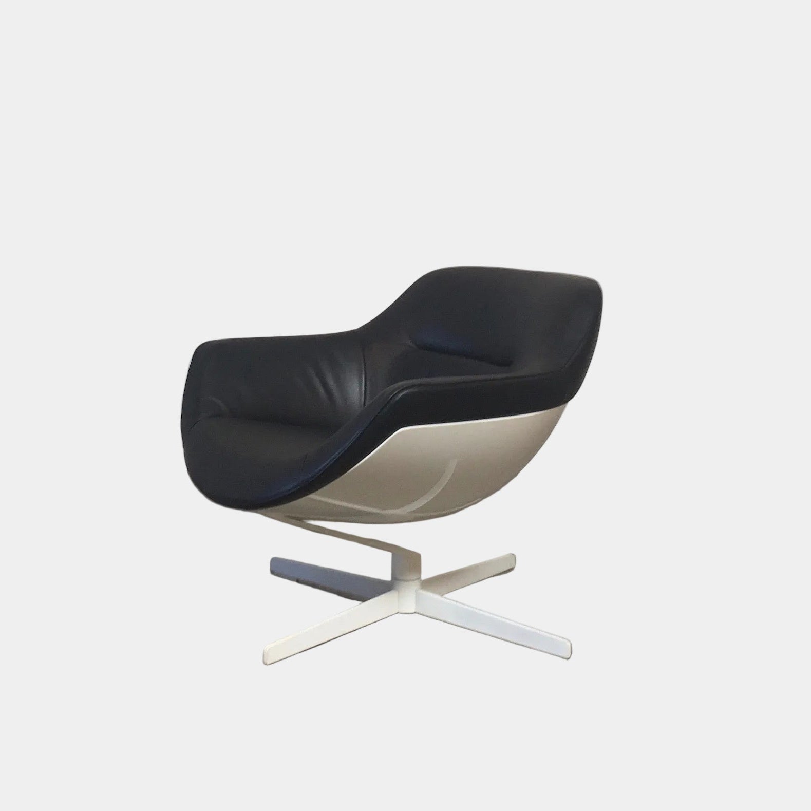 Cassina Auckland Swivel Lounge Chair by Jean-Marie Massaud, featuring a modern black and white curved seat with a metal base, is showcased on a concrete floor against a plain white background.