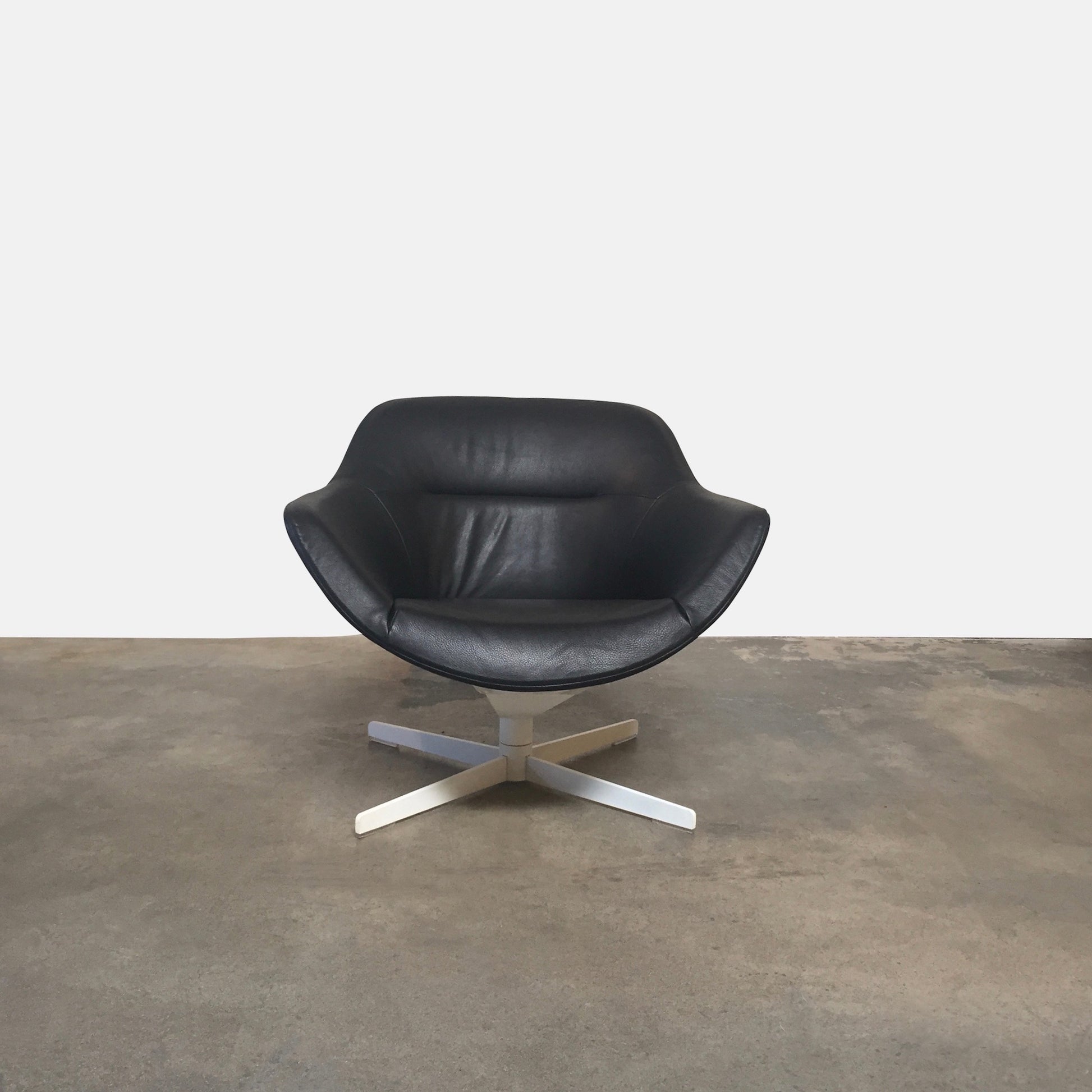 Cassina Auckland Swivel Lounge Chair by Jean-Marie Massaud, featuring a modern black and white curved seat with a metal base, is showcased on a concrete floor against a plain white background.