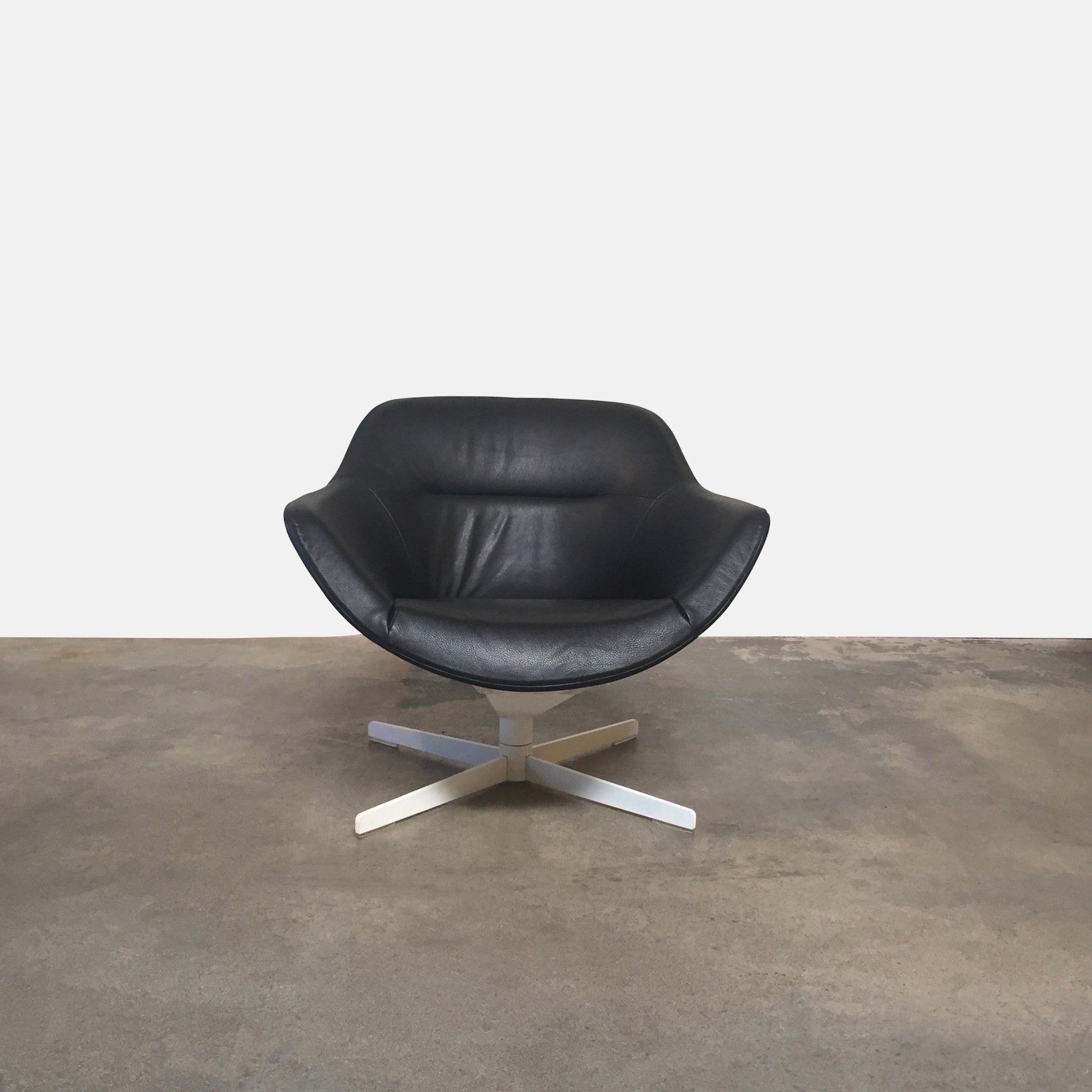 Cassina Auckland Swivel Lounge Chair by Jean-Marie Massaud, featuring a modern black and white curved seat with a metal base, is showcased on a concrete floor against a plain white background.