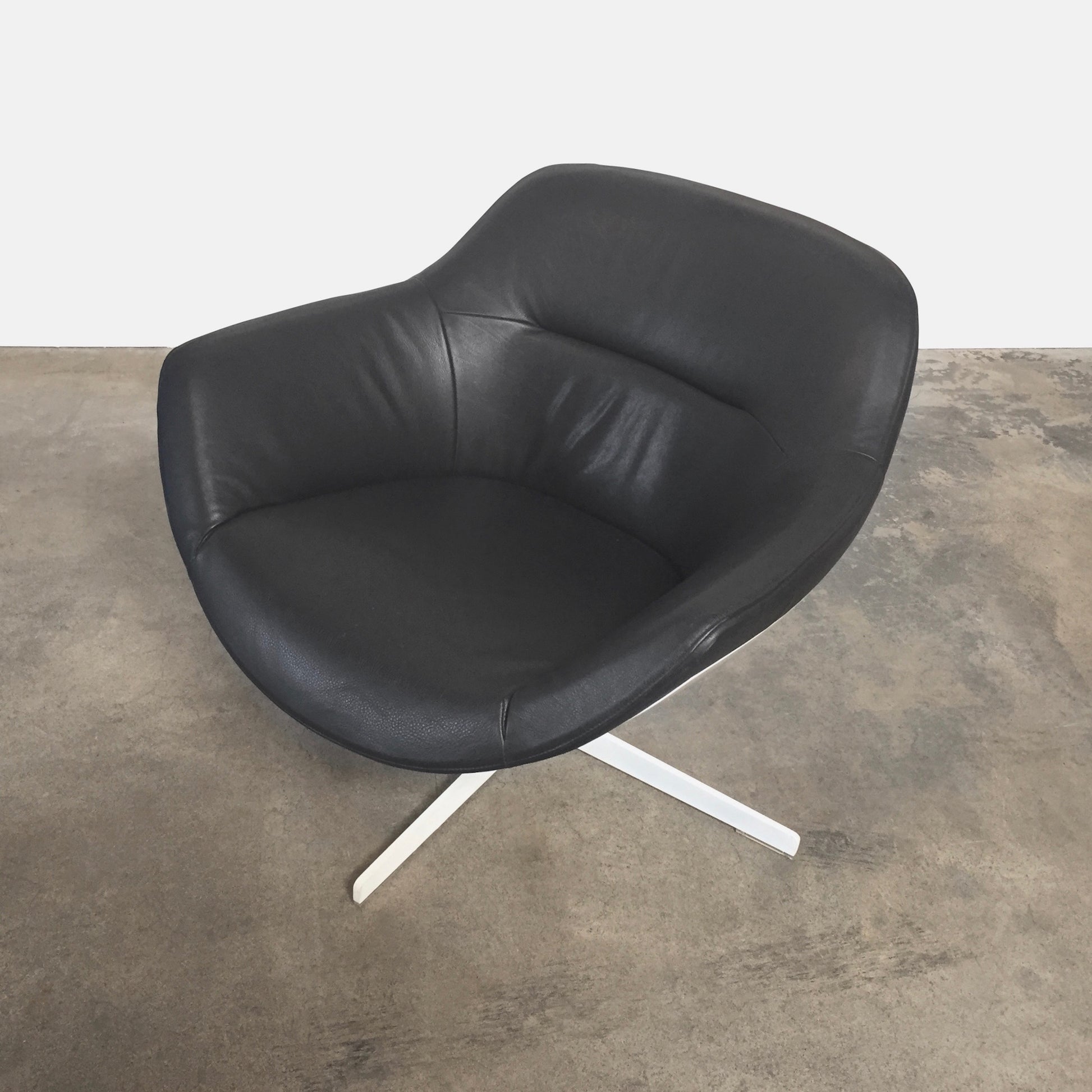 Cassina Auckland Swivel Lounge Chair by Jean-Marie Massaud, featuring a modern black and white curved seat with a metal base, is showcased on a concrete floor against a plain white background.