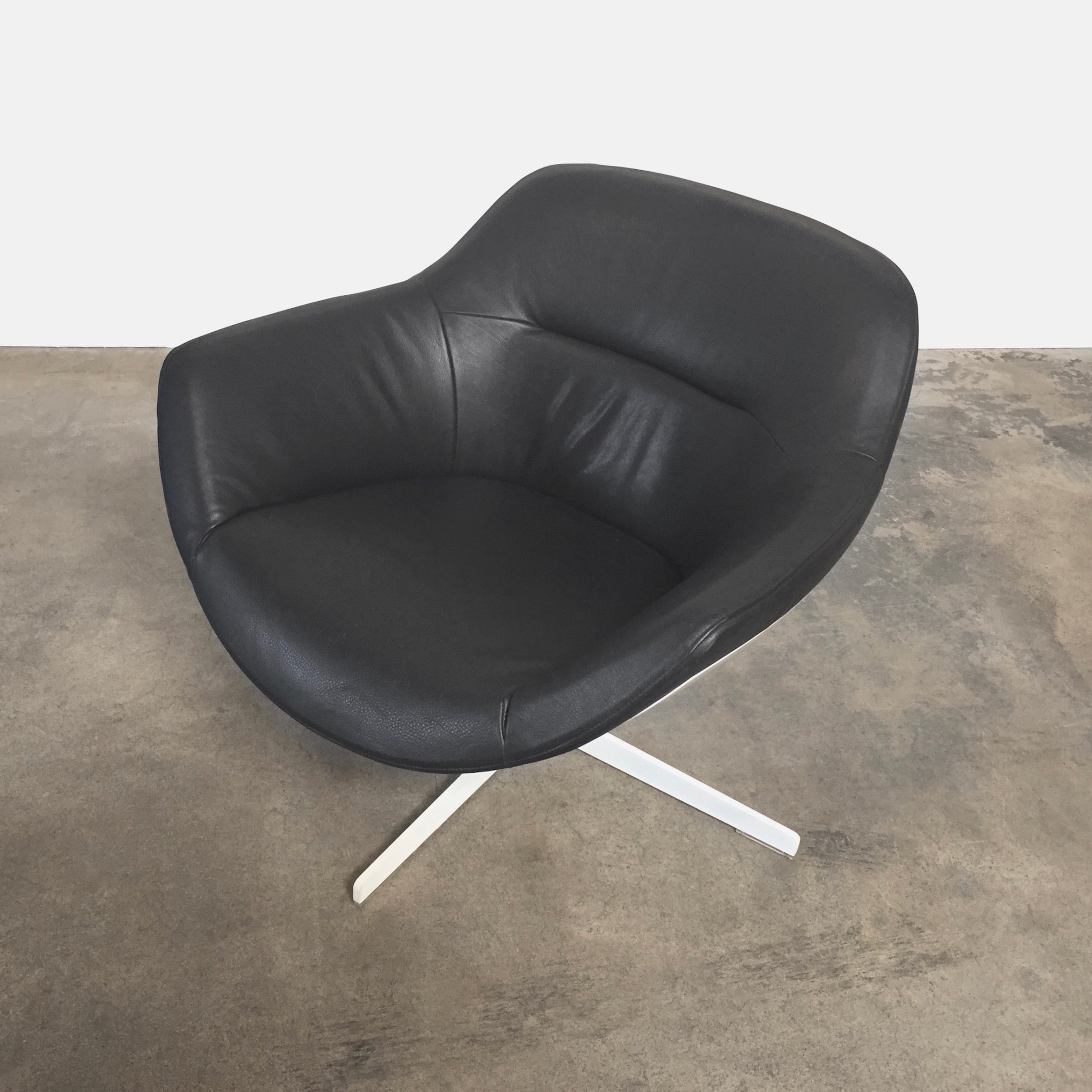 Cassina Auckland Swivel Lounge Chair by Jean-Marie Massaud, featuring a modern black and white curved seat with a metal base, is showcased on a concrete floor against a plain white background.