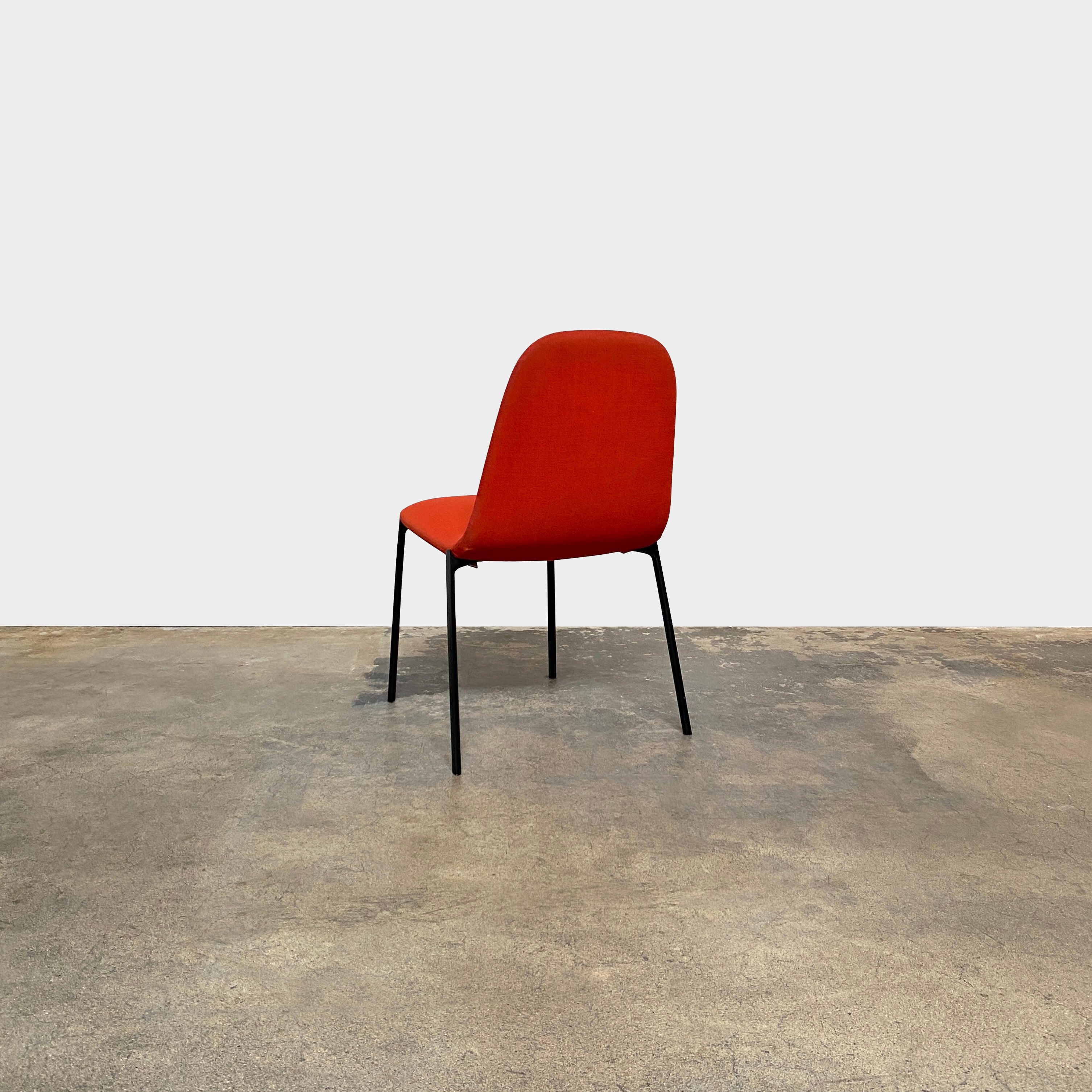 Four Zanotta Ella Dining Chairs, with their red fabric and black metal legs, are set in a row against a plain white background, showcasing the sleek design of this Italian brand.